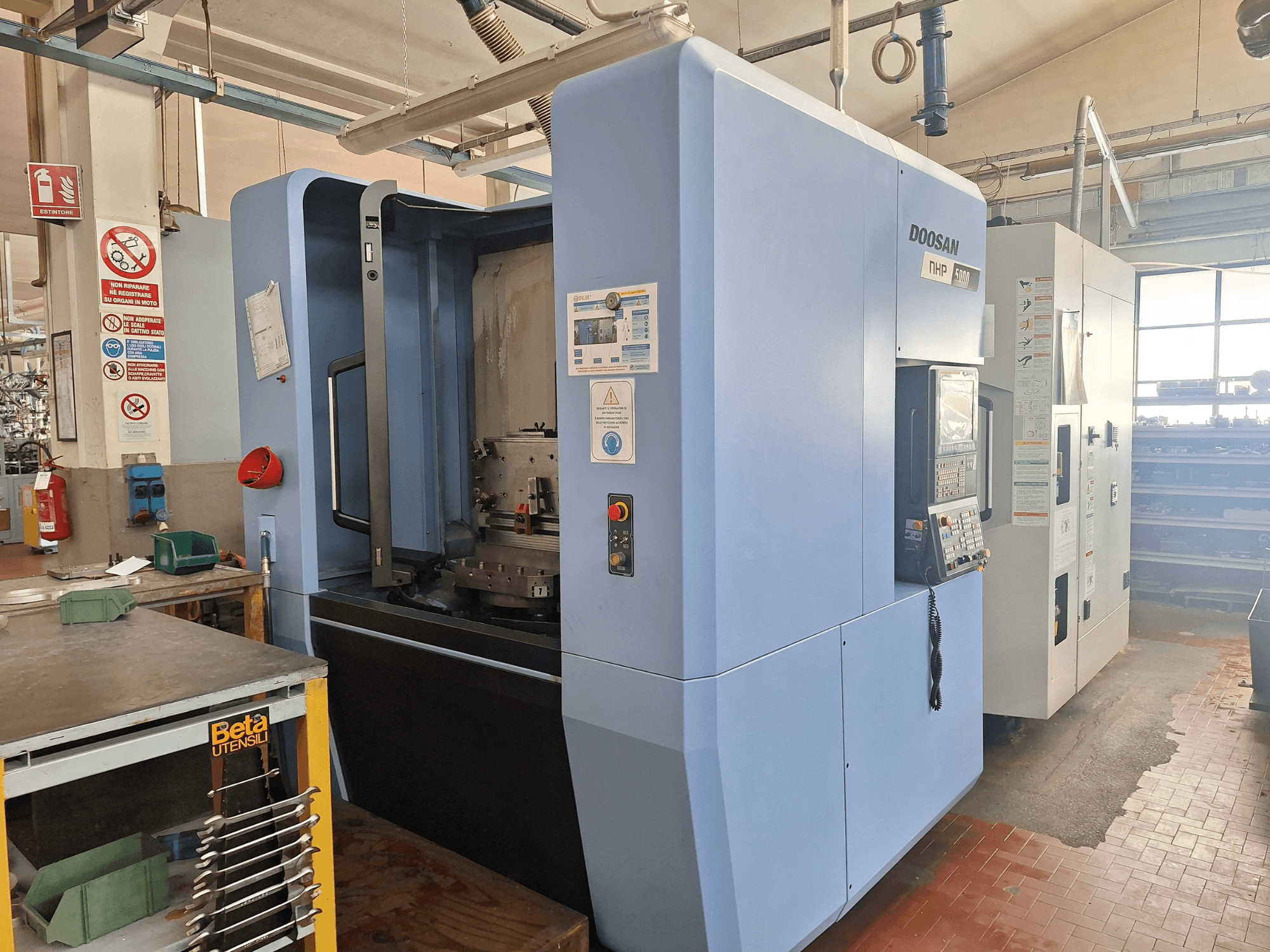 Centre d'usinage horizontal DOOSAN NHP 5000 dans un atelier, vue latérale montrant le panneau de commande et la zone d'usinage.