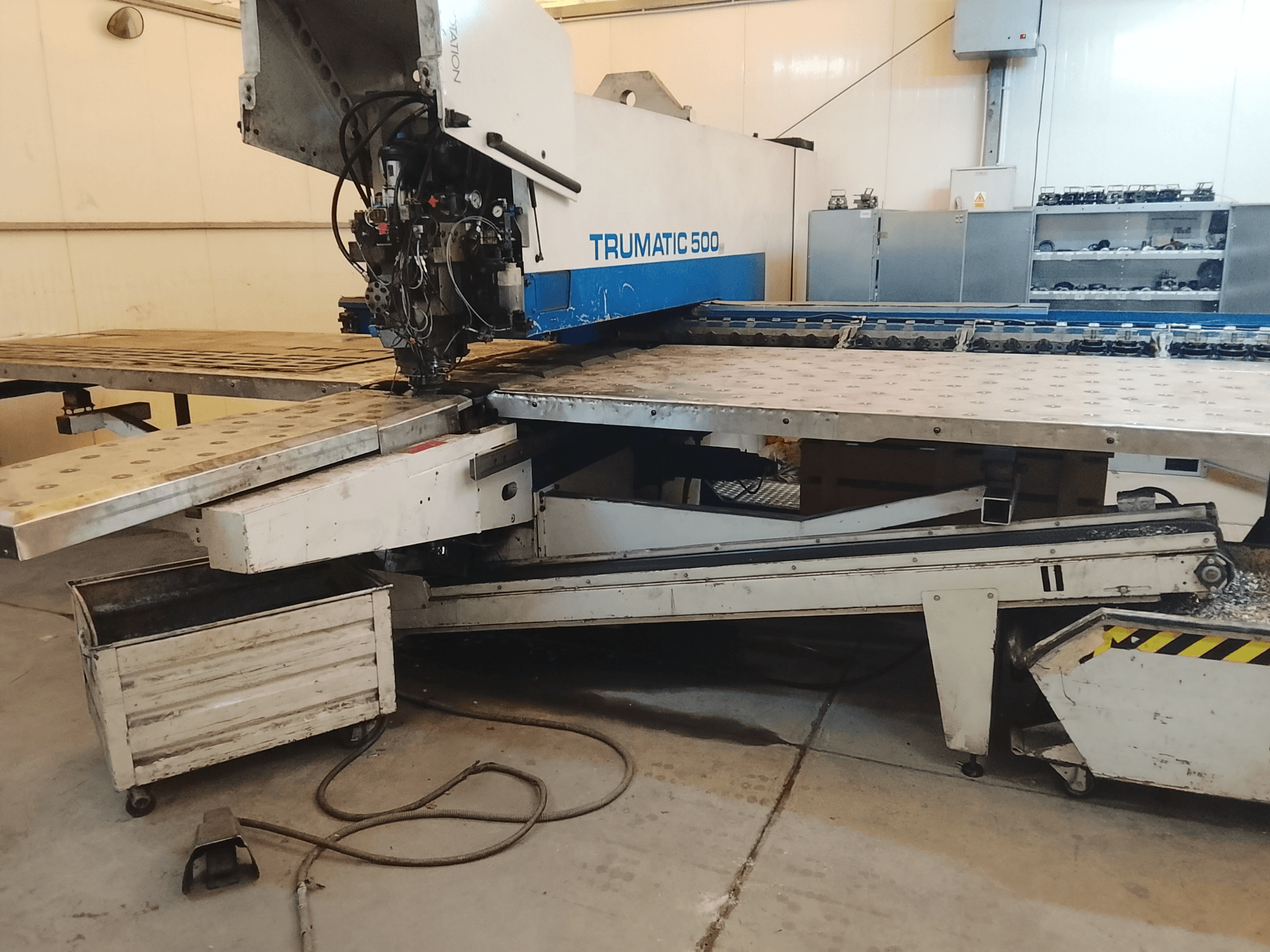 Machine CNC TRUMATIC 500 dans un atelier, vue latérale montrant la tête de coupe et la table de travail métallique avec des trous pré-percés.