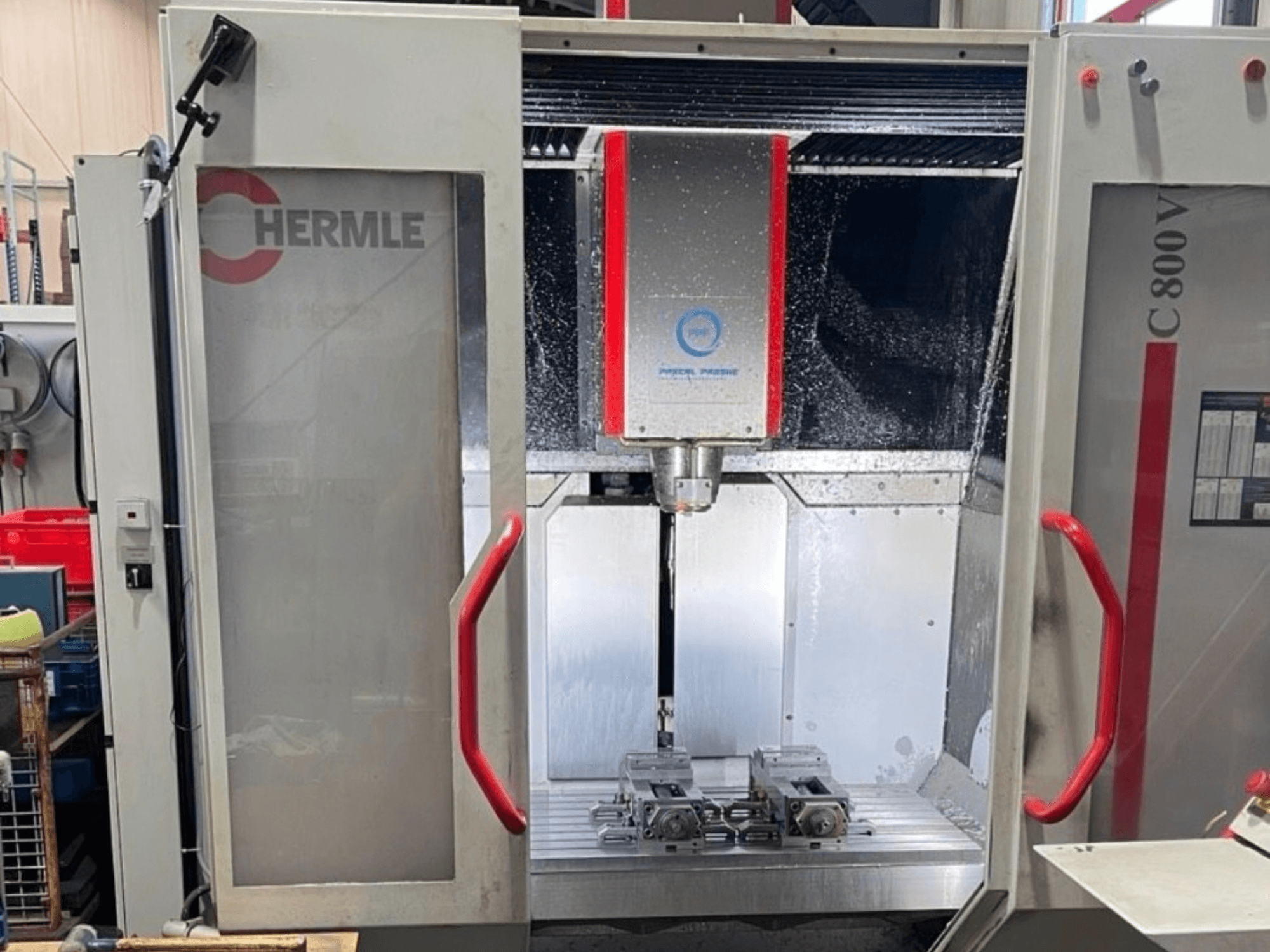 Centre d'usinage vertical HERMLE C800V, vue de face montrant la zone d'usinage avec les pièces et le liquide de refroidissement.