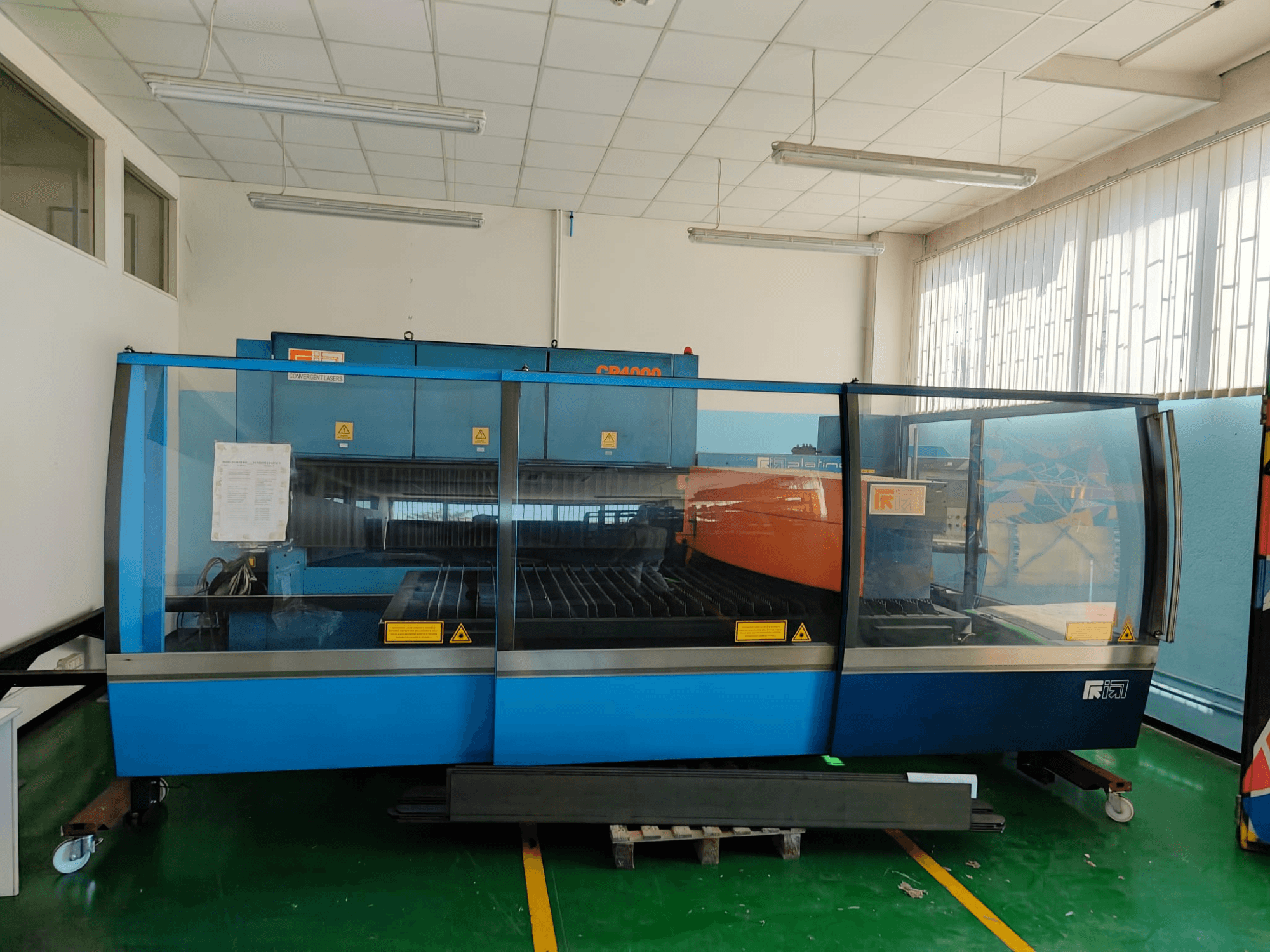 Vue de face d'une machine de découpe laser CO₂ CONVERGENT LASERS CP4000, arborant un motif bleu et orange, dans un atelier bien éclairé.