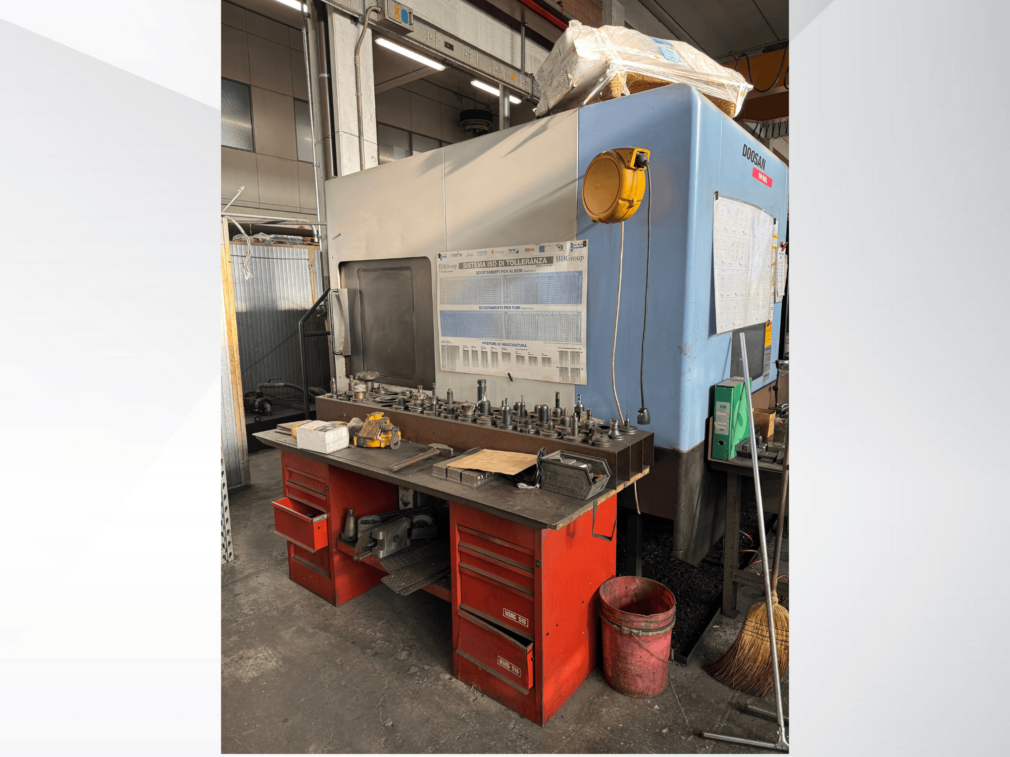 Centre d'usinage Doosan avec un établi rouge et un espace de rangement, présentant les outils et l'équipement, vu de face.