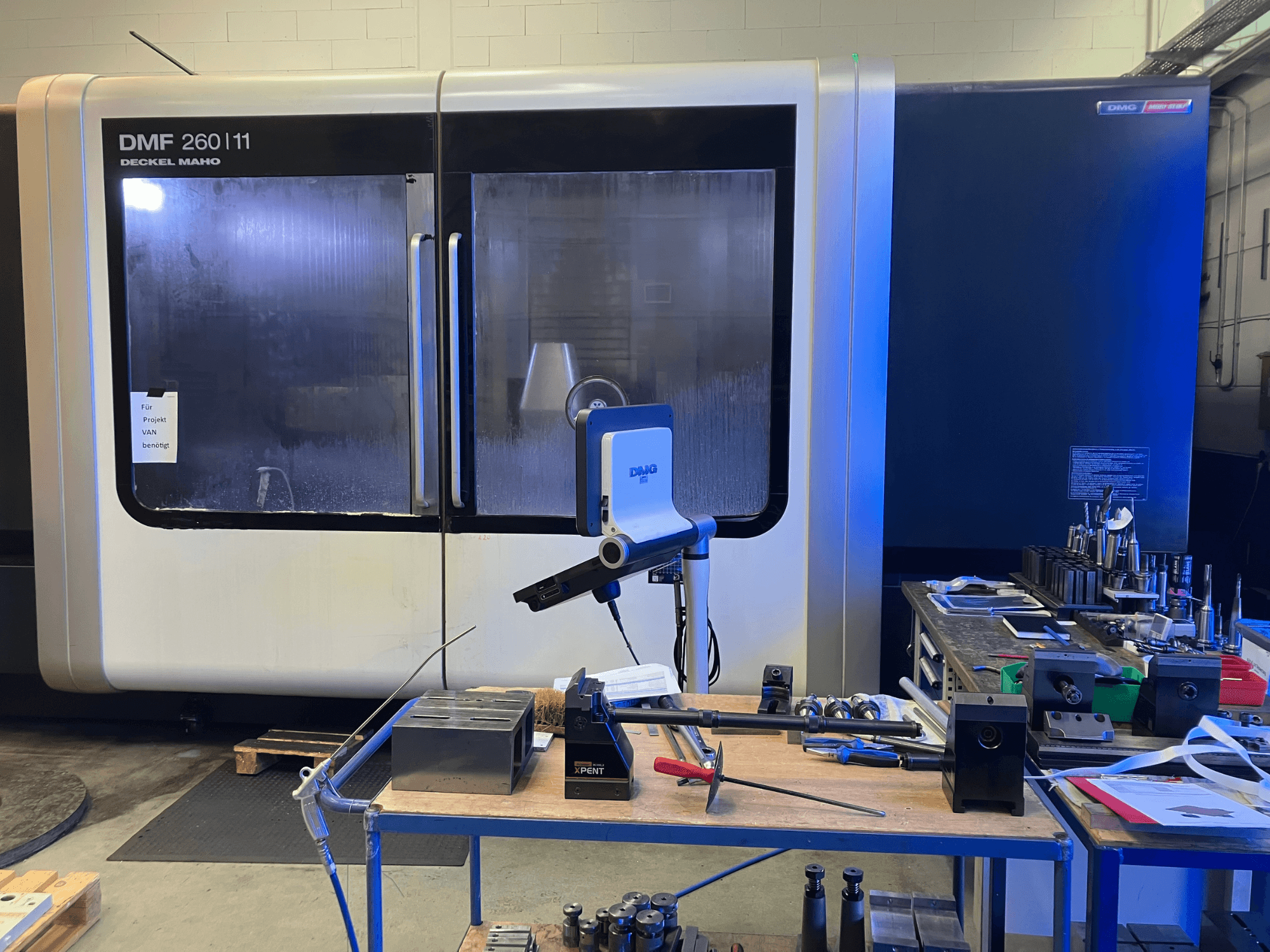 Vue de face du centre d'usinage vertical DMG DECKEL MAHO DMF 260|11 avec outils et matériaux sur un poste de travail.