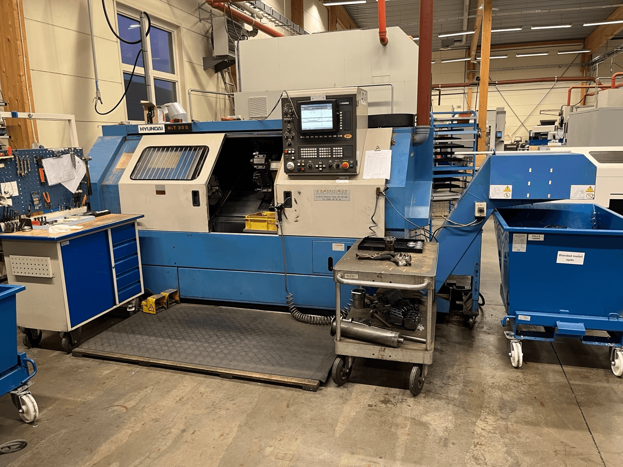 Tour horizontal Hyundai HIT 30S, vue de face, avec panneau de commande et outils sur un chariot à proximité dans un atelier.