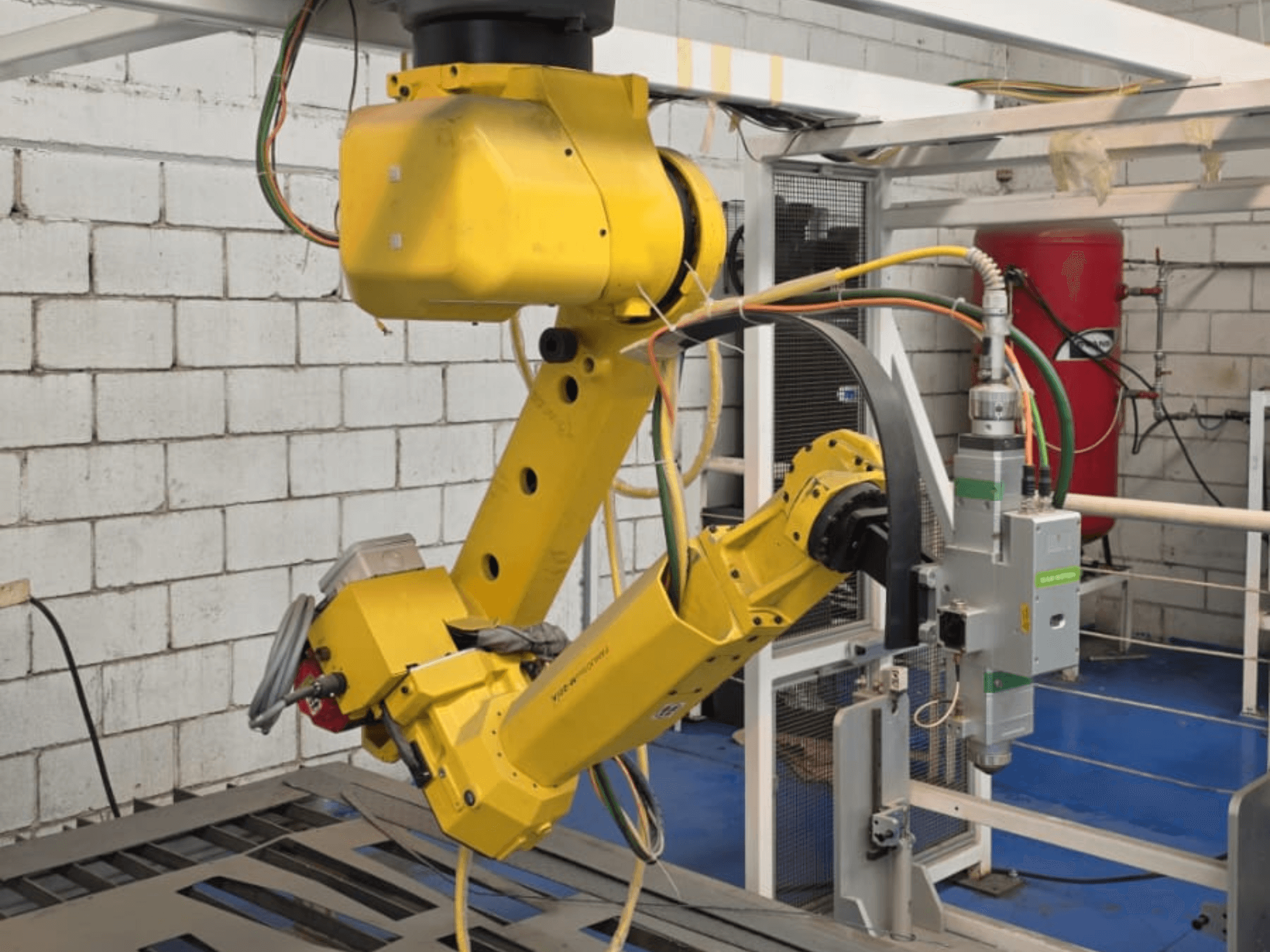 Bras robotisé jaune avec un outil de précision, doté de multiples articulations et câbles, vu de face dans un environnement industriel.