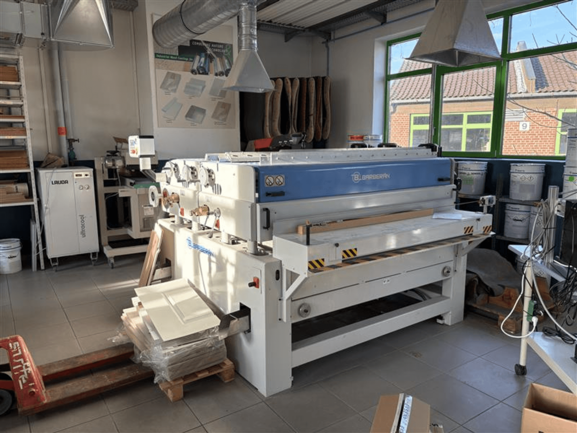 Machine à travailler le bois Blaserbn dans un atelier, vue de face ; avec des panneaux de bois sur une palette et un équipement moderne à l'arrière-plan.