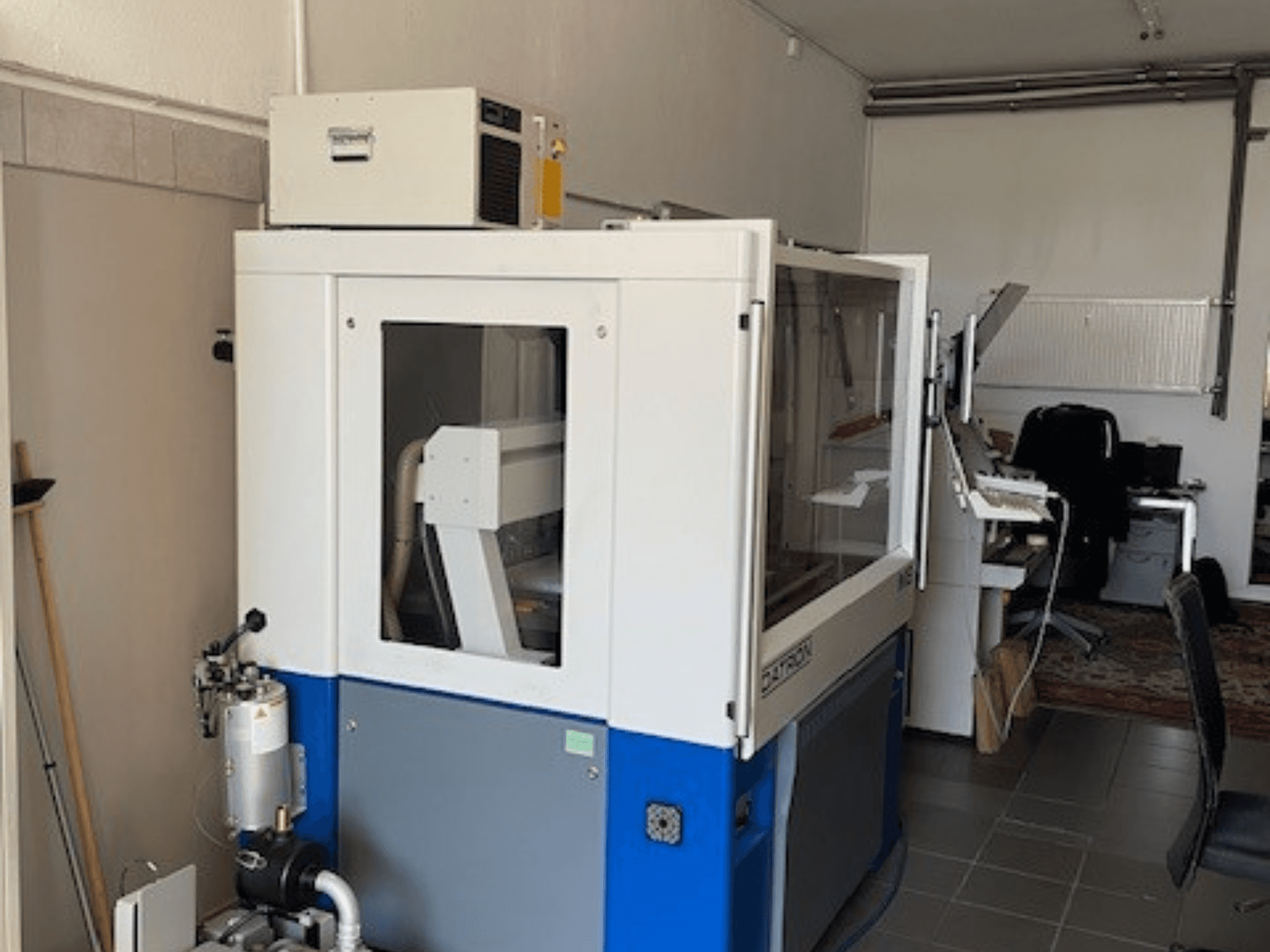 Machine industrielle bleue et blanche avec panneaux transparents, vue de face, comprenant l'accès aux commandes et l'unité de ventilation visible.