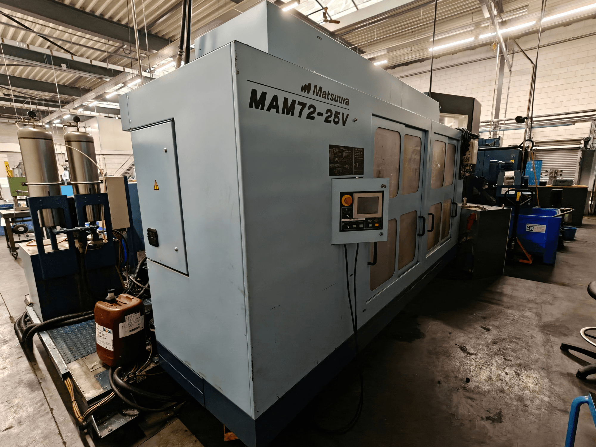 Machine CNC Matsuura MAM72-25V, vue de côté, avec panneau de commande, deux réservoirs de liquide de refroidissement et espace de travail dans un environnement industriel.