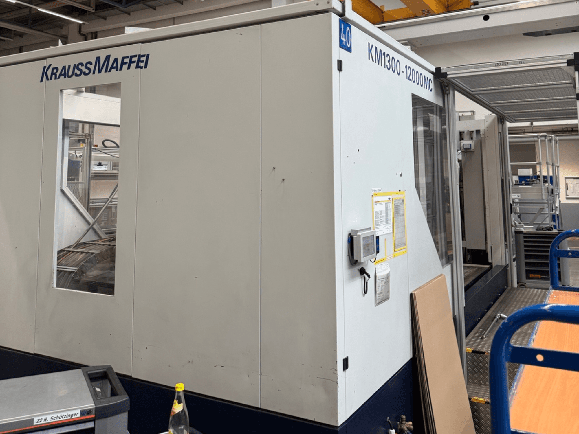 Machine de moulage par injection hydraulique Krauss Maffei KM1300-12000 MC, vue latérale, présentant le panneau de commande et l'espace opérationnel.