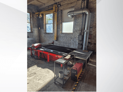 Table de découpe plasma CNC rouge avec panneau de commande et conduit d'évacuation métallique, vue de côté dans un atelier bien éclairé.