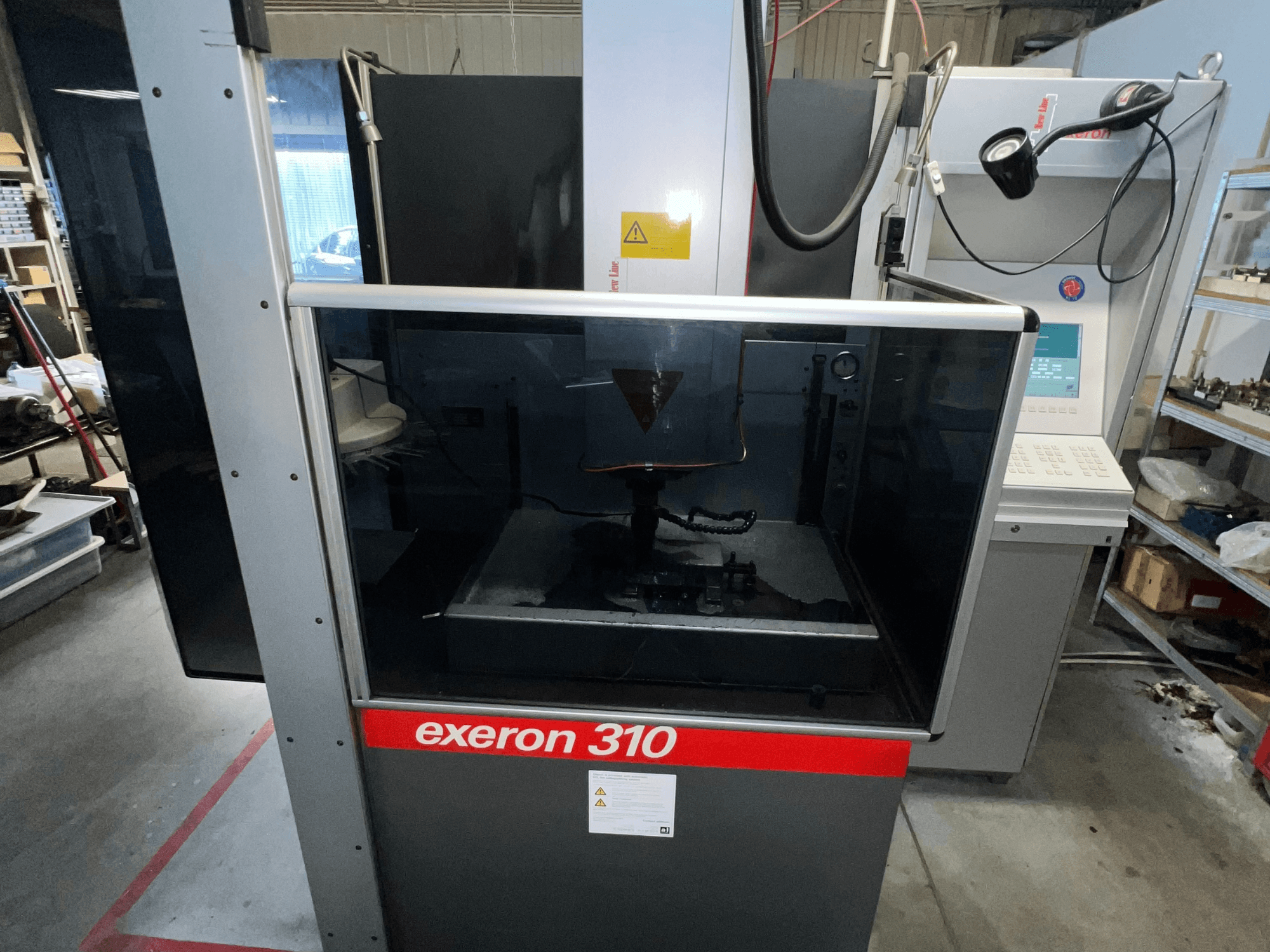 Vue avant d'une machine Exeron 310, montrant une chambre en verre et un panneau de contrôle à côté des étagères du poste de travail.