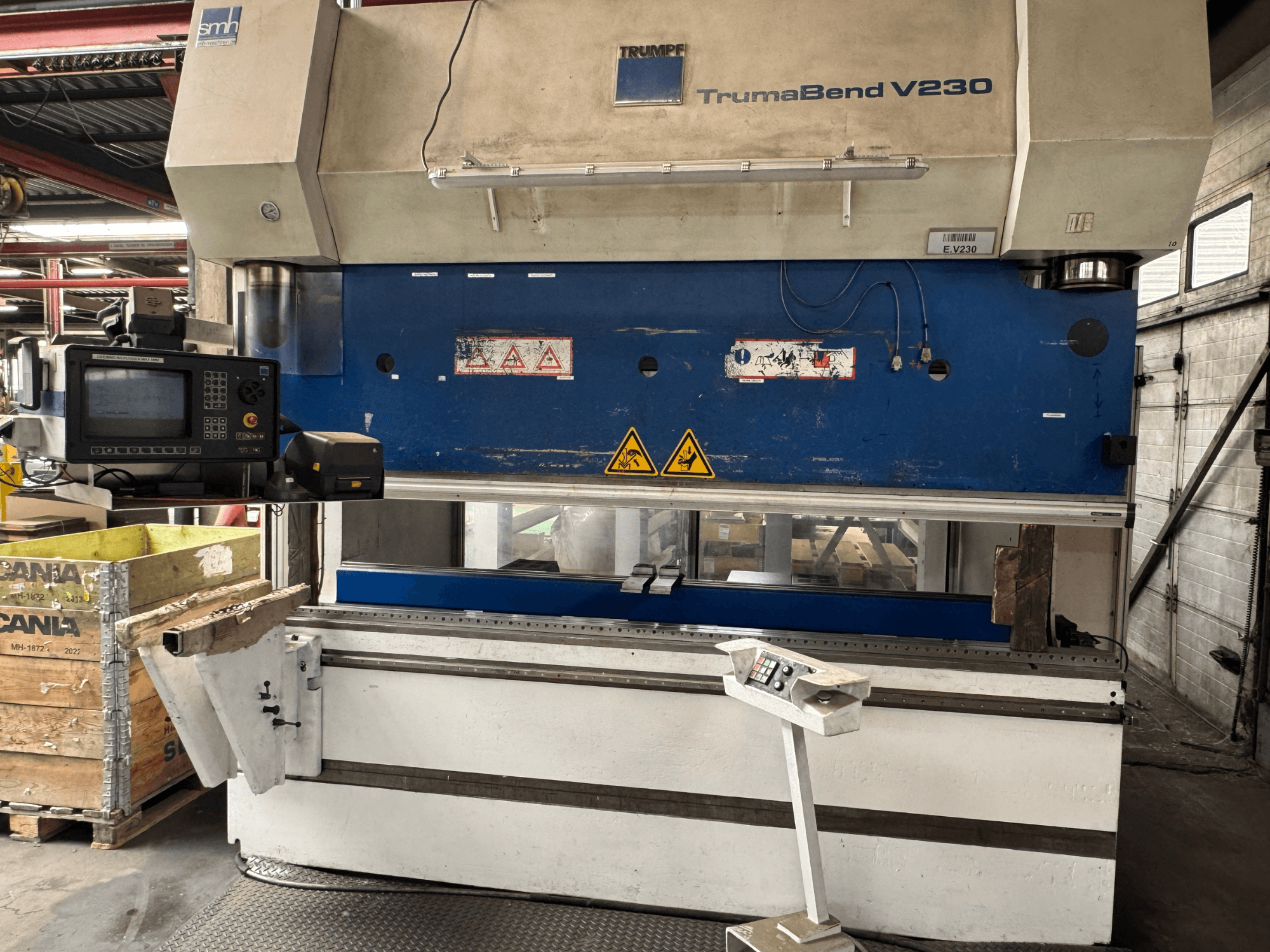Presse plieuse TRUMPF TrumaBend V230, vue de face avec panneau de commande, étiquettes d'avertissement et bras de support de la pièce visible.