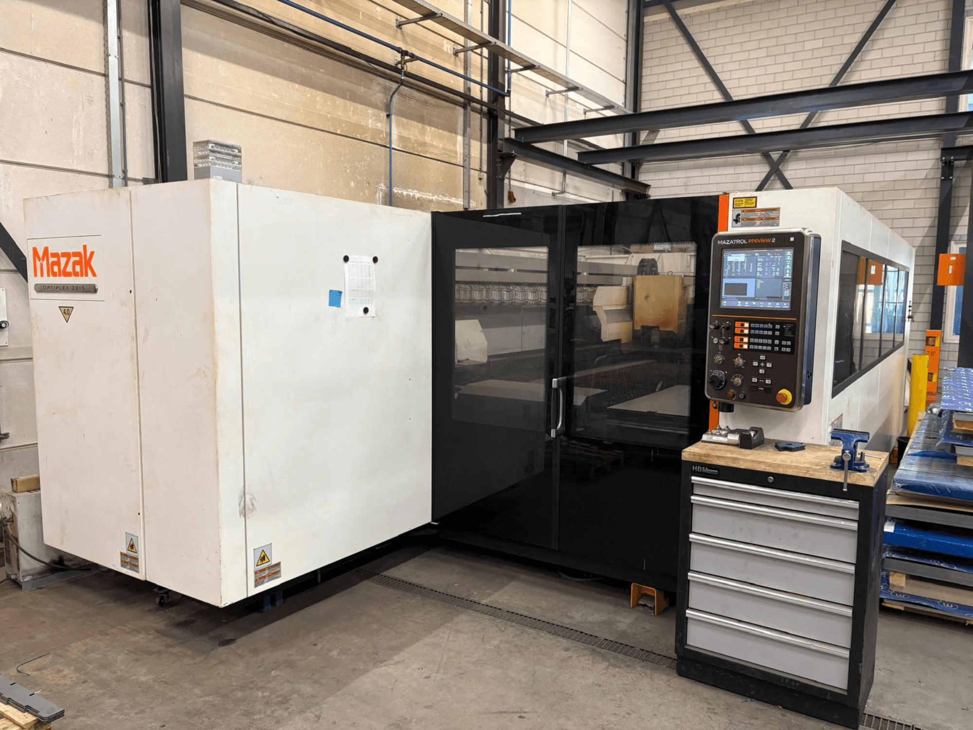 Machine de découpe laser CO₂ Mazak Optiplex 3015, vue de face, montrant le panneau de commande et l'environnement industriel.