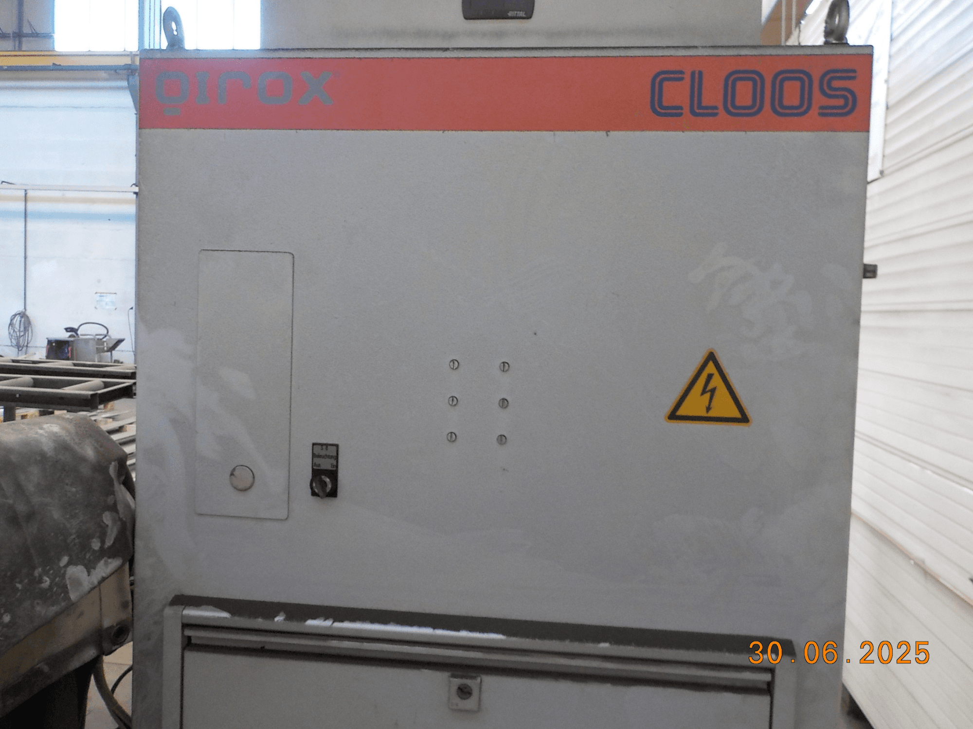 Vue latérale de la machine à souder Cloos QIROX, avec le panneau de commande et le panneau d'avertissement, avec une surface poussiéreuse et un tampon de date visible.