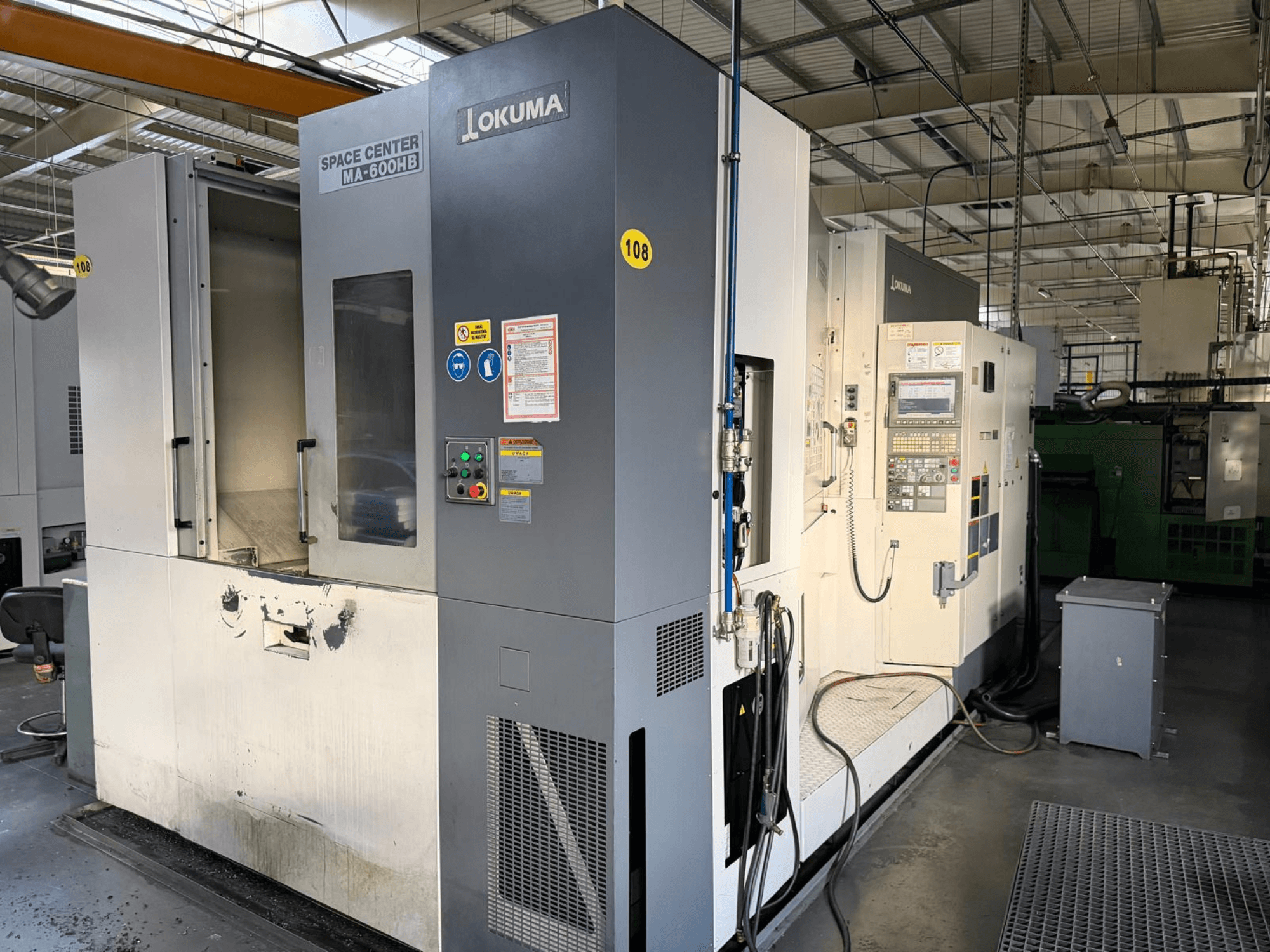 Centre d'usinage horizontal Okuma MA-600 HB, vue de face, montrant le panneau de commande et la zone de coupe avec des marques d'usure visibles.