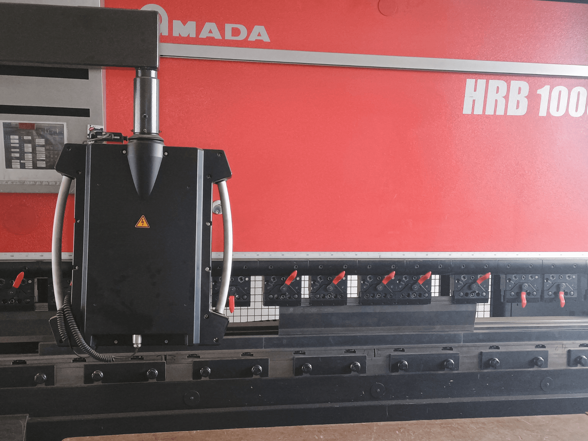Vue de face de la cintreuse Amada HRB 100 ; elle est équipée d'une tête de commande noire avec une buse conique et des pinces réglables.