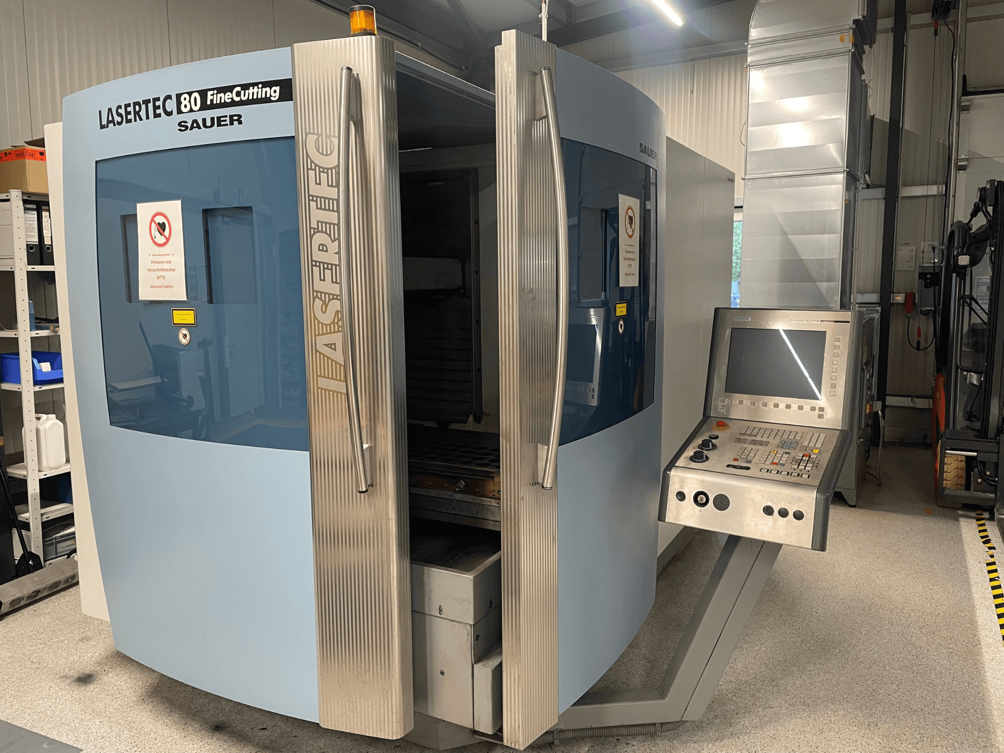 Vue de face de la machine de découpe de tôles DMG Sauer Lasertec80 FineCutting, avec son panneau de commande, ses portes ouvertes et ses panneaux de sécurité bien visibles.