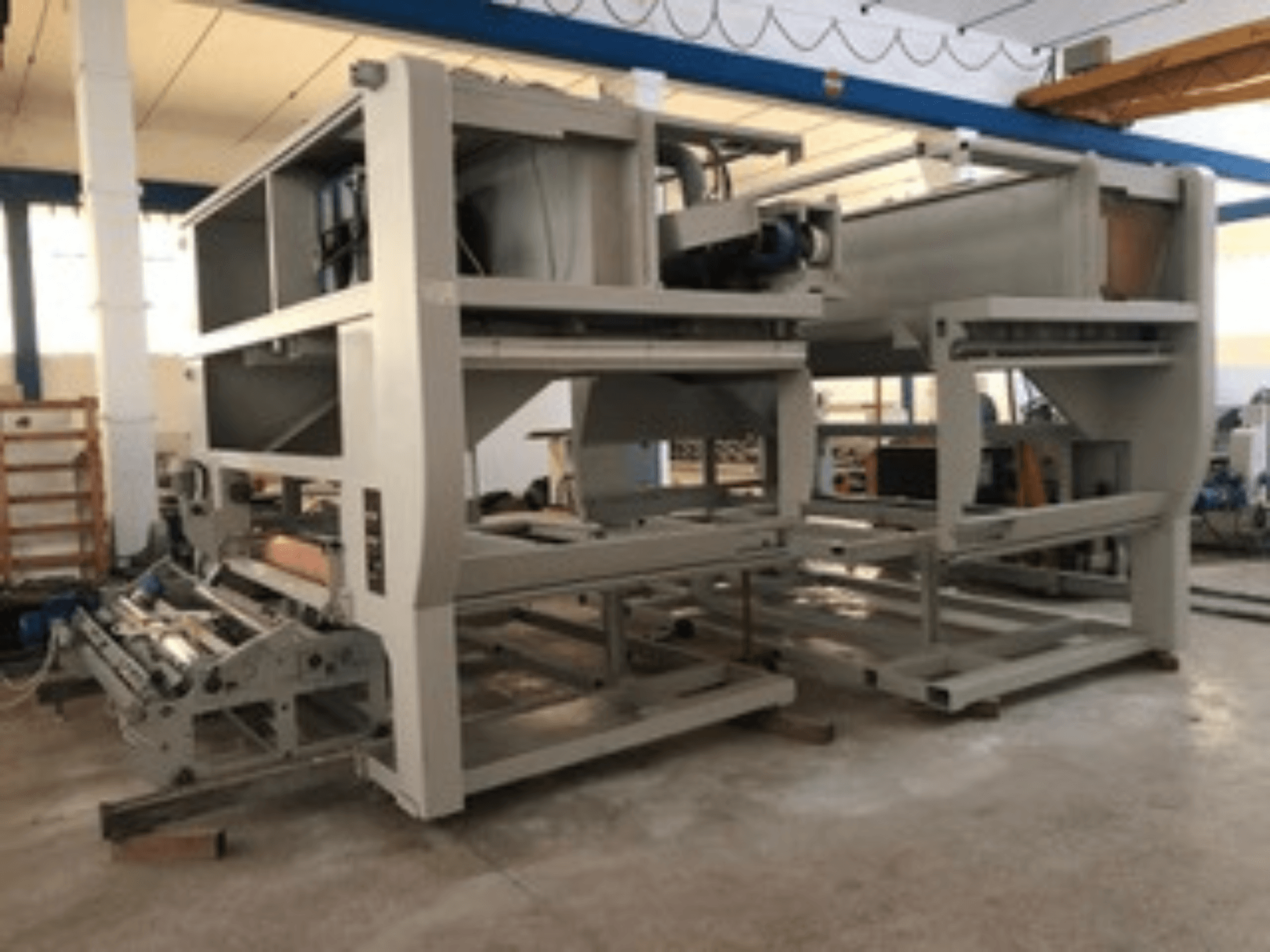 Machine industrielle avec plusieurs rouleaux de convoyage et une grande structure ; vue latérale, couleur grise, située dans une usine bien éclairée.