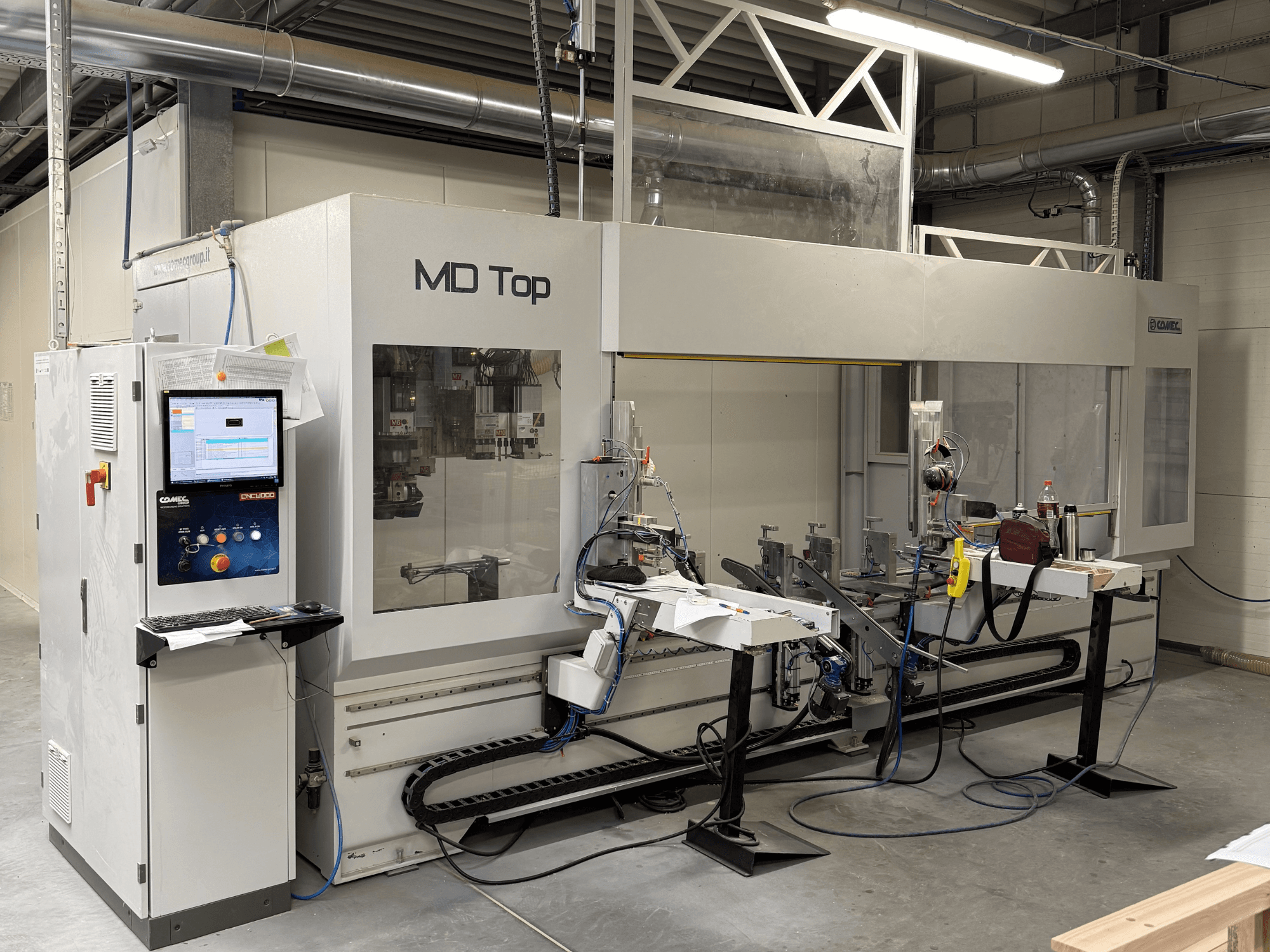 Machine CNC MD Top vue de face, comportant un panneau de commande, des bras robotisés et un espace de travail avec des outils et des matériaux.