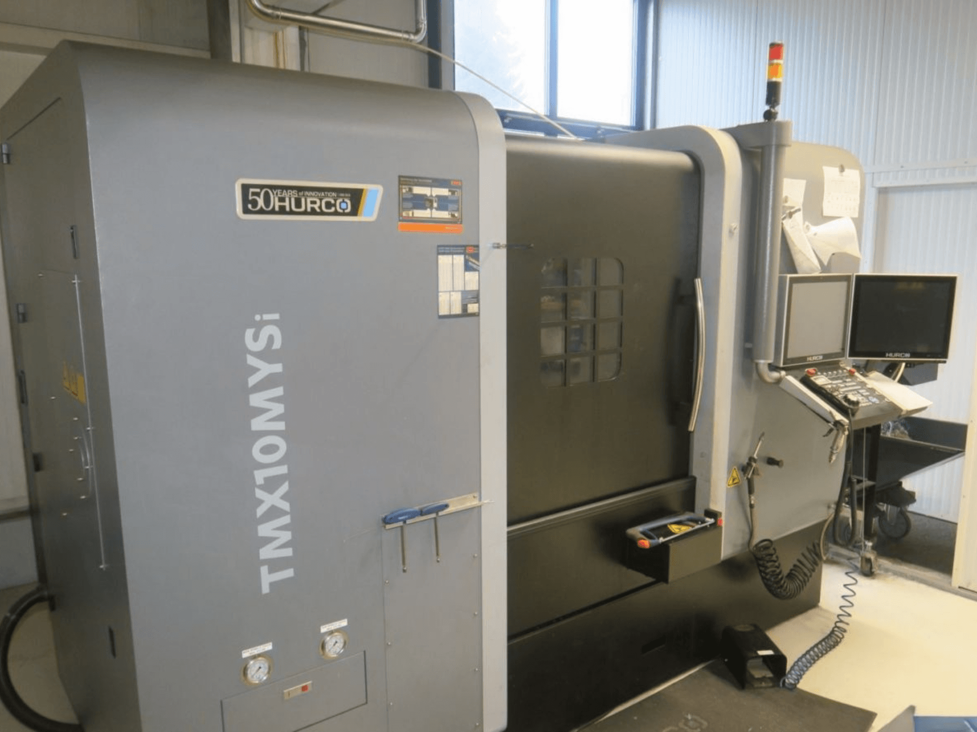 Machine CNC Hurco TMX10MYSi vue de côté ; le panneau de commande, les lumières d'urgence et les jauges sont affichés.