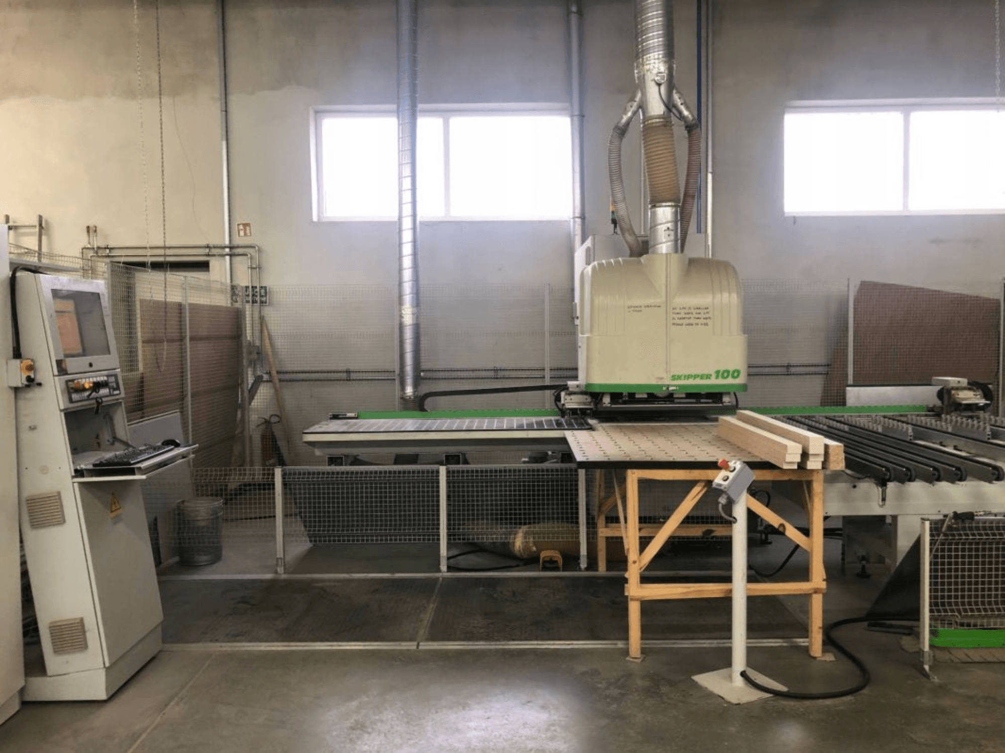 Centre d'usinage CNC BIESSE SKIPPER 100 dans un atelier ; la vue de face montre la machine avec son panneau de commande et du bois posé sur la table.