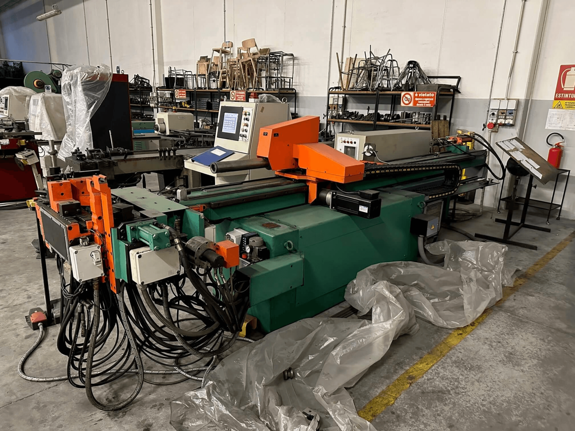 Machine industrielle avec un corps orange et vert, un panneau de commande et de nombreux câbles, vue de face dans un atelier.