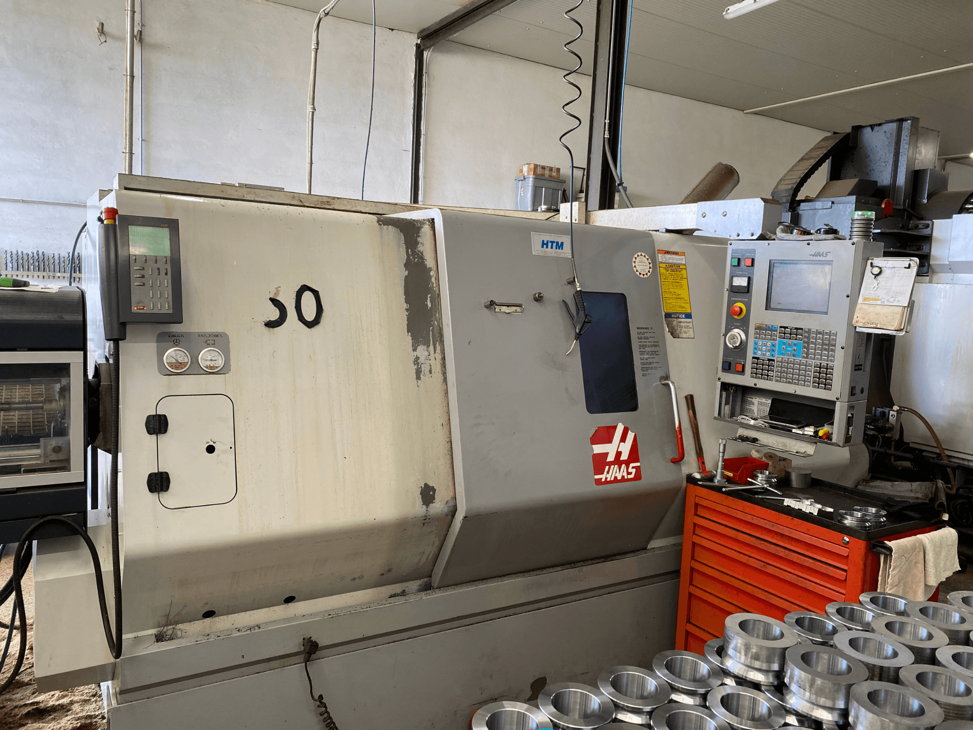 Machine CNC Haas avec panneau de commande, vue de face, montrant les boutons de commande, les jauges et les pièces métalliques empilées à proximité.