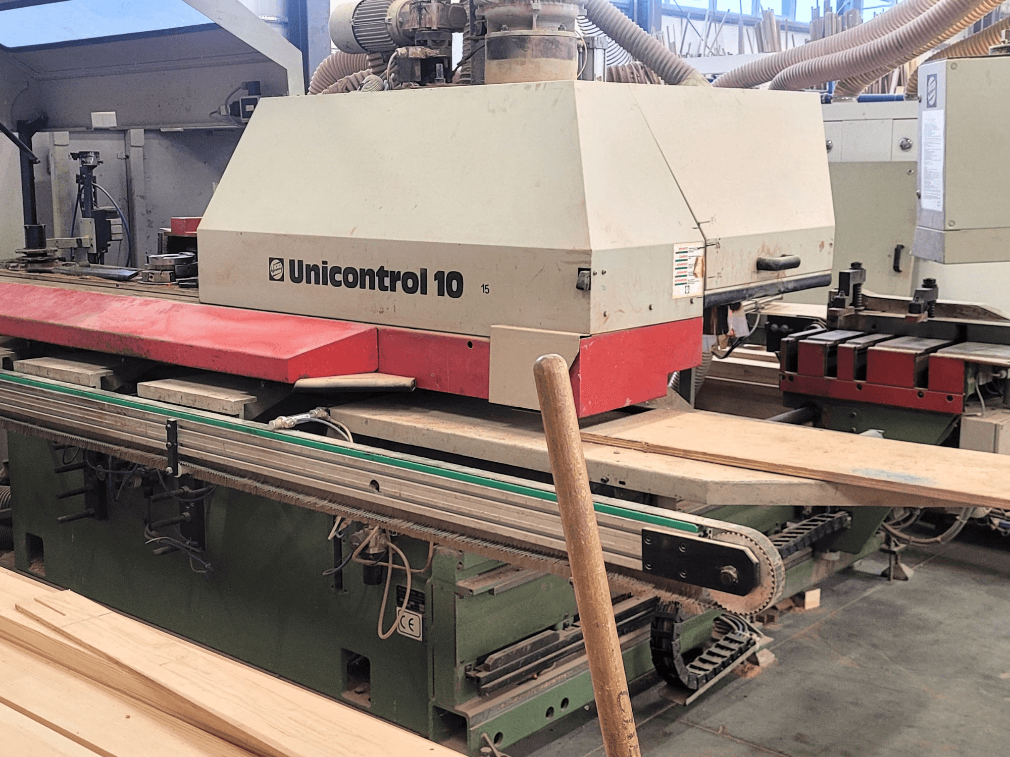 Centre d'usinage CNC Unicontrol 10 de WEINIG/DIMTER, vue de face avec des planches en bois et des équipements dans un atelier.