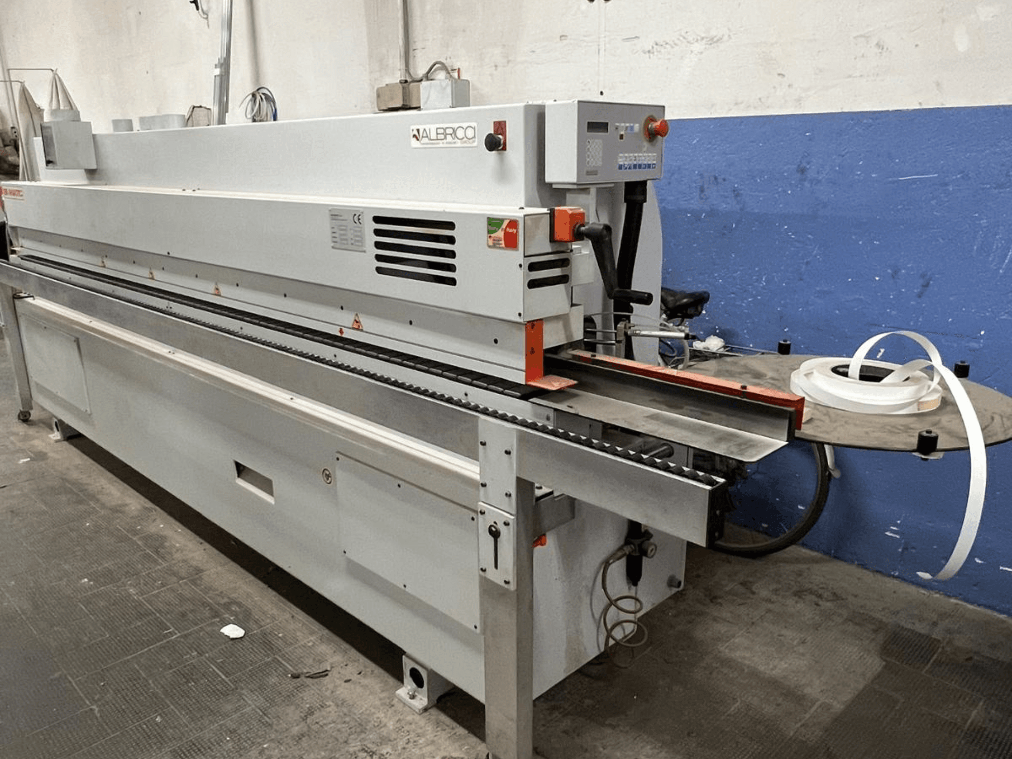 Plaqueuse de chants ALBRICO vue de face, avec un long convoyeur et un rouleau de ruban adhésif.