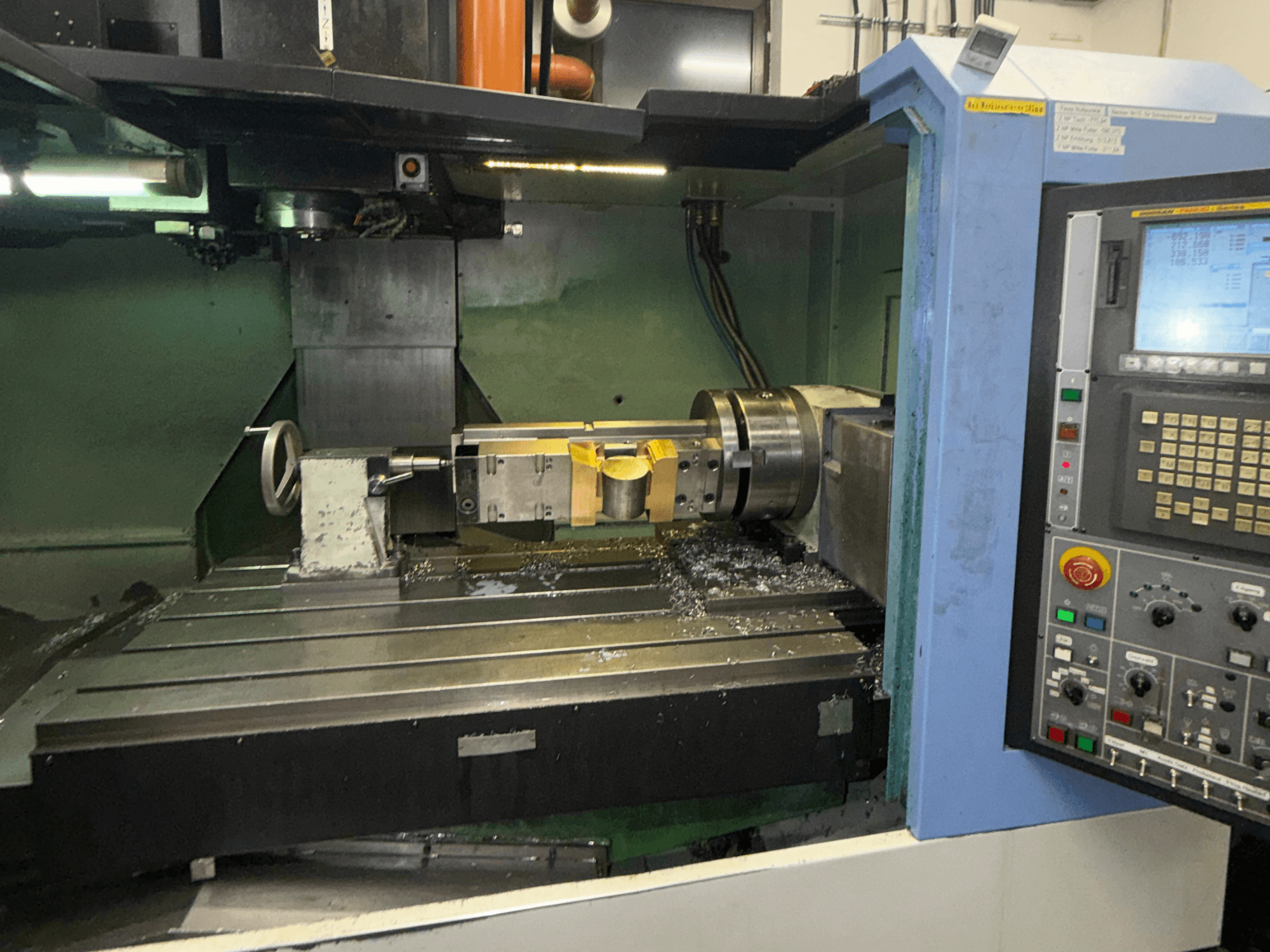 Centre d'usinage vertical DOOSAN DNM650, vue de face, mettant en évidence l'outil de coupe et le panneau de commande, avec des copeaux métalliques visibles sur la table.