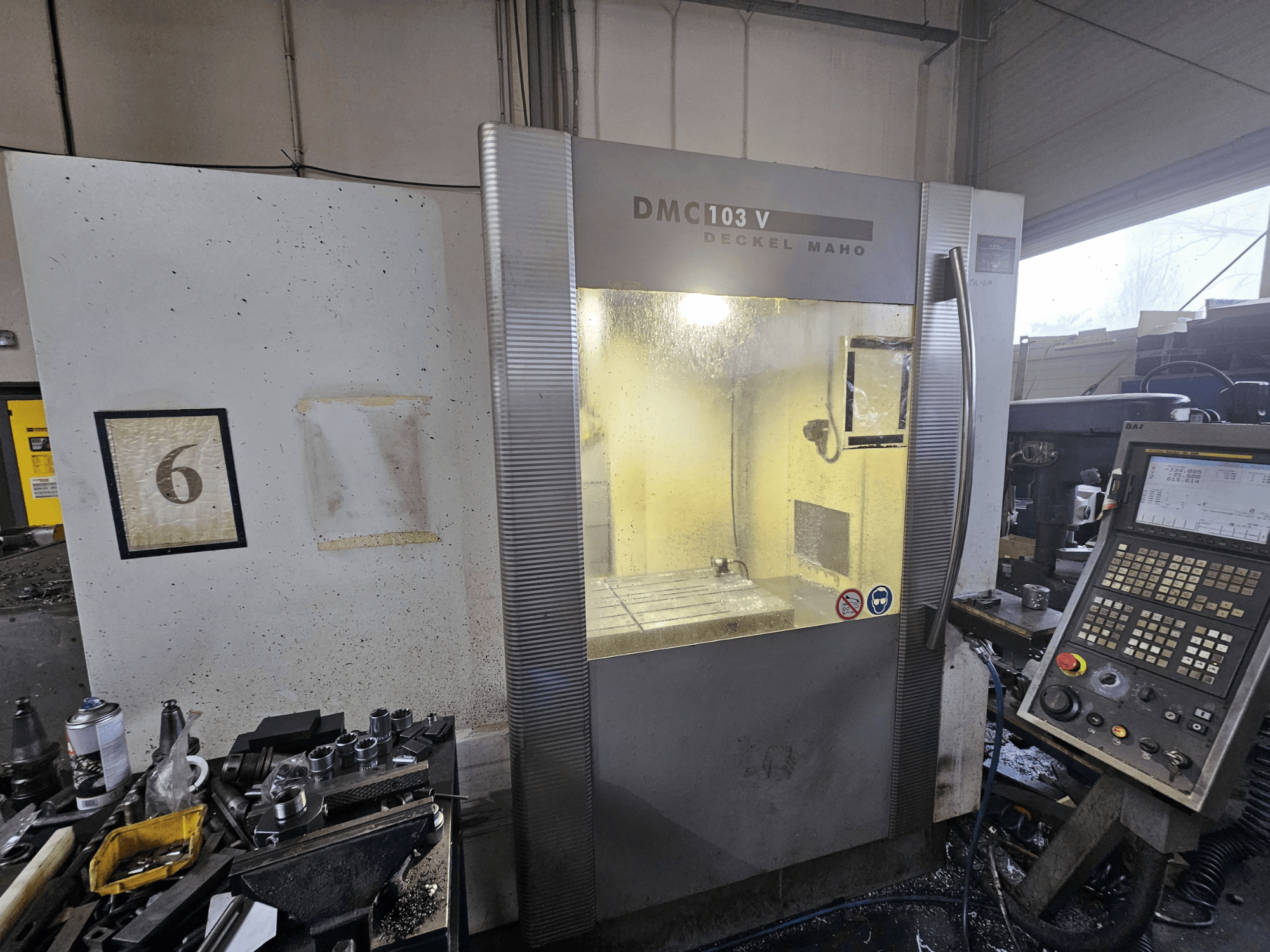 Machine CNC Deckel Maho DMC 103 V, vue de face, avec le panneau de commande et l'espace de travail, avec un numéro "6" sur le mur.