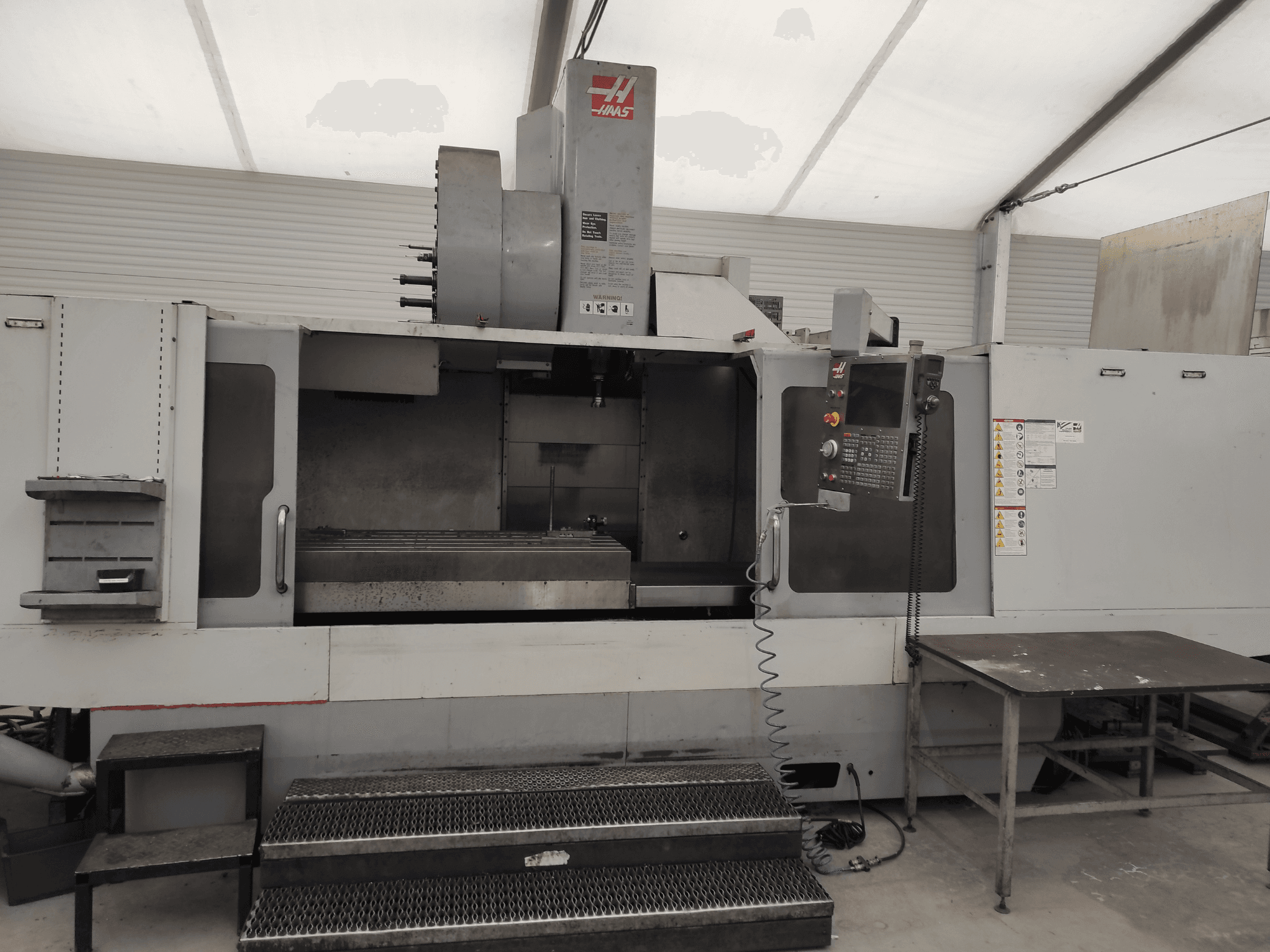Centre d'usinage vertical HAAS VF-10/50HE, vue de face montrant le panneau de commande, le banc de la machine et la marche accessible pour l'opération.