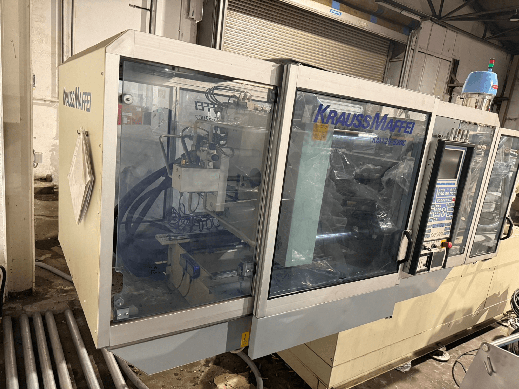 Machine de moulage par injection hydraulique Krauss Maffei KM125-520C2, vue de face avec panneau de commande et boîtier transparent.