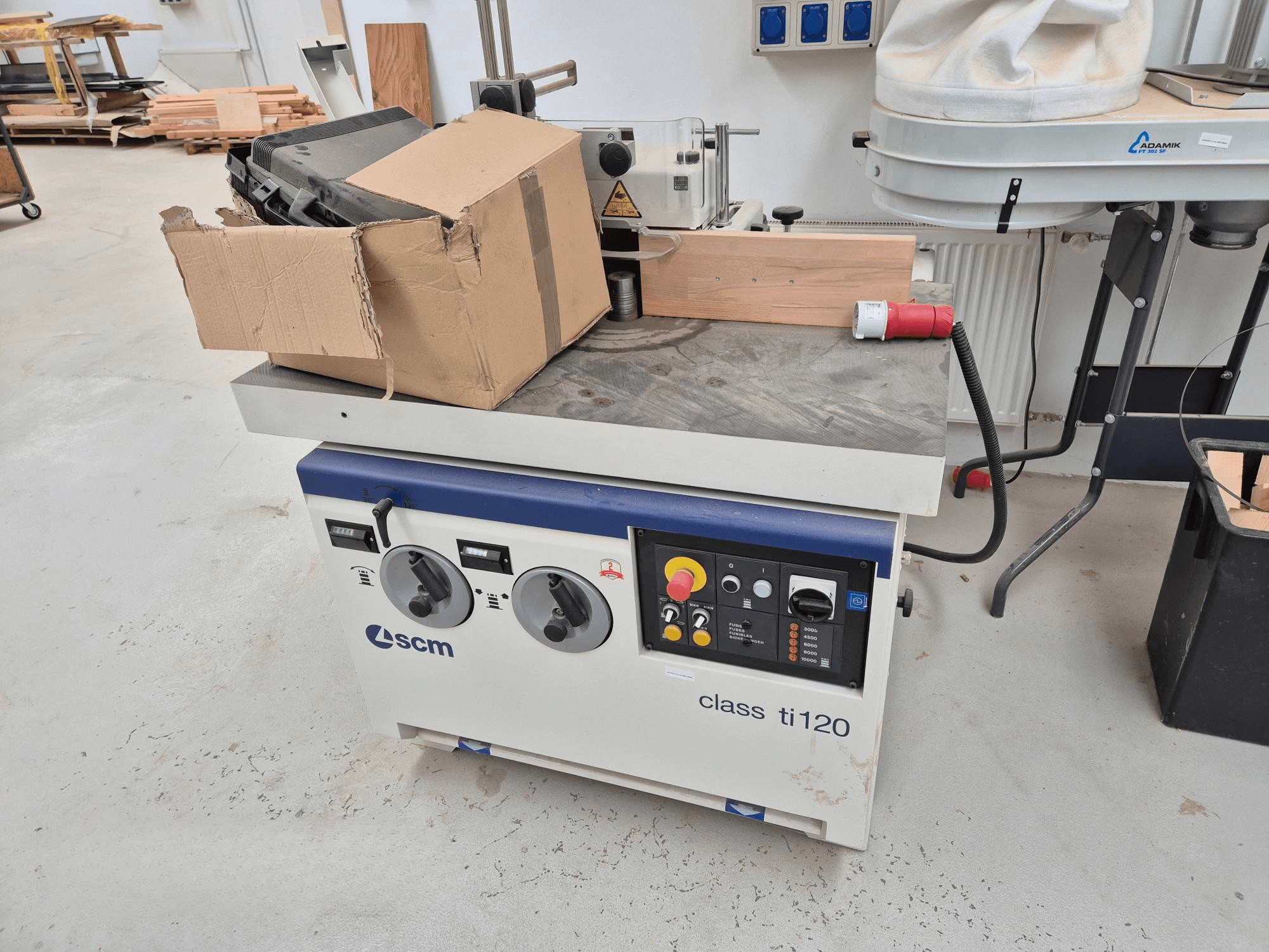 Machine à travailler le bois SCM classe ti120, vue de face, comportant un panneau de commande avec des boutons et une boîte en carton.