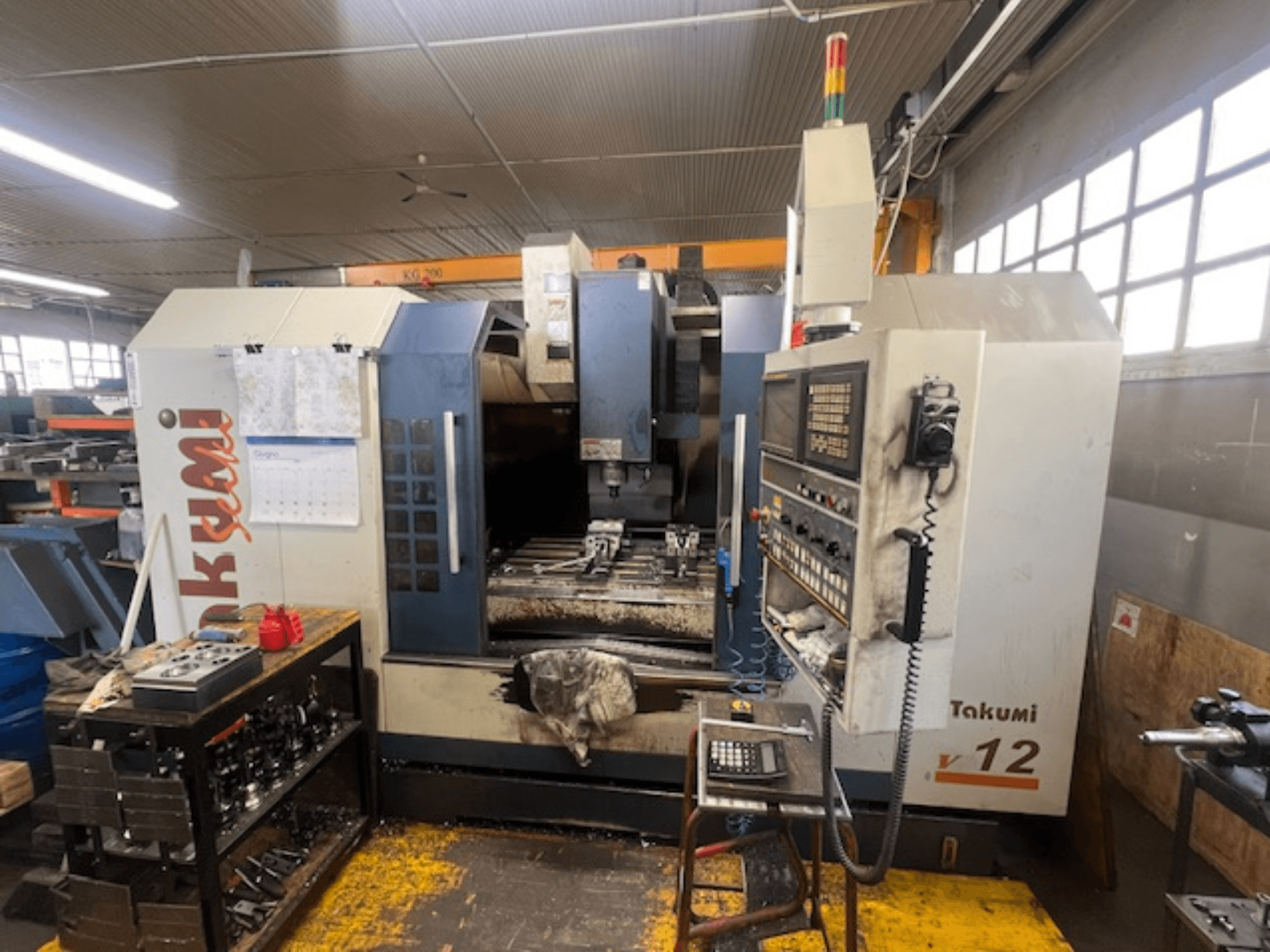 Fraiseuse Takumi V12 CNC en vue latérale, montrant le panneau de commande, la zone de coupe et les outils sur la station de travail.