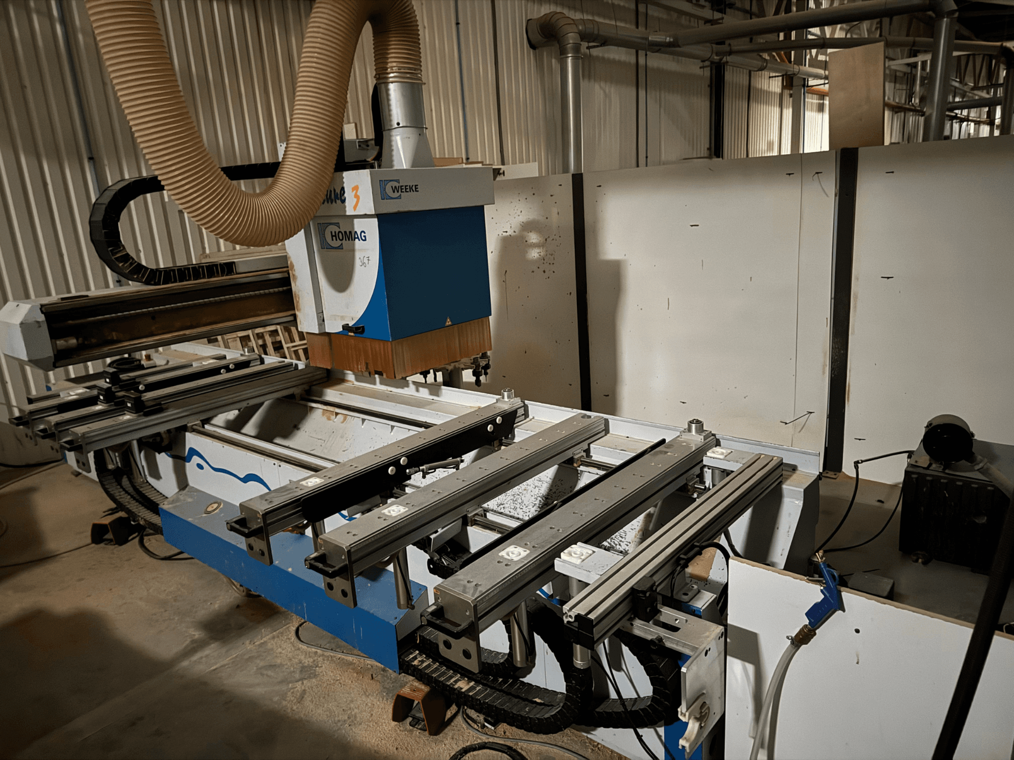 La machine CNC HOMAG au design bleu et blanc, vue de côté, est équipée de rails coulissants, d'un système d'aspiration des poussières et d'outils montés.