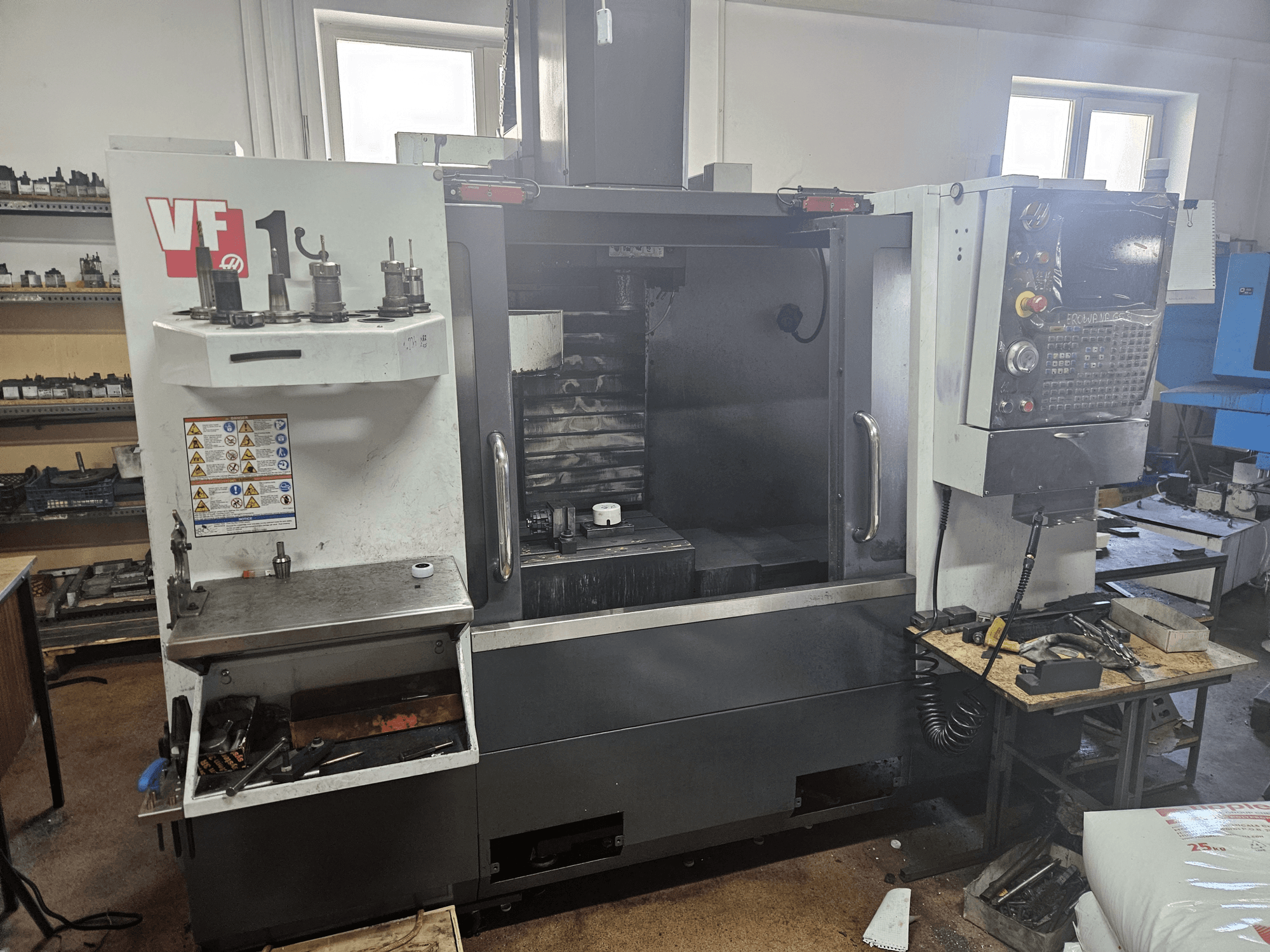Centre d'usinage vertical HAAS VF-1, vue de face avec les outils sur le côté, le panneau de commande visible et l'espace de travail à l'arrière-plan.