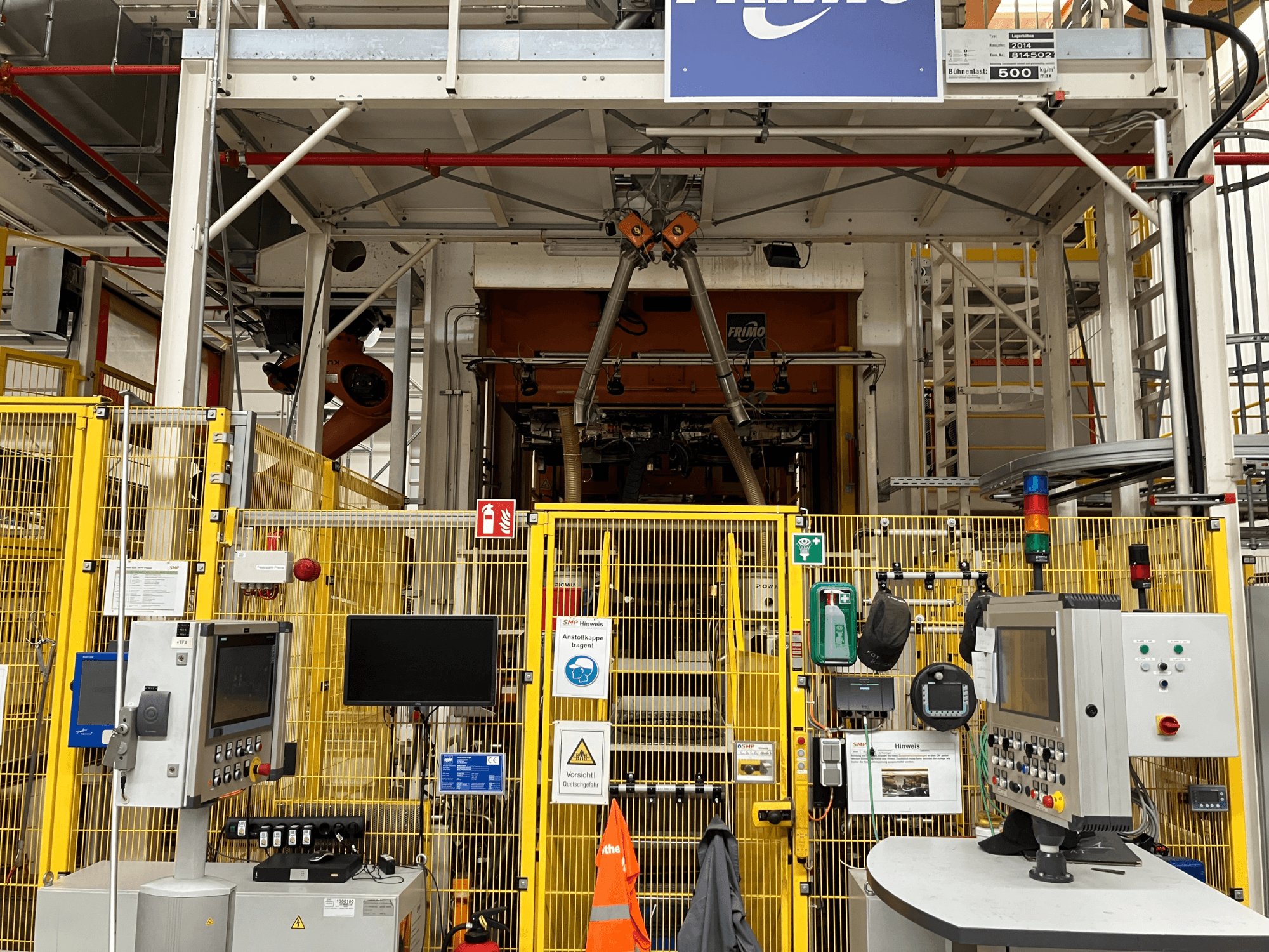 Vue avant de l'usine de thermoformage FRIMO NFPP, avec panneaux de commande et clôtures de sécurité dans un environnement industriel bien éclairé.