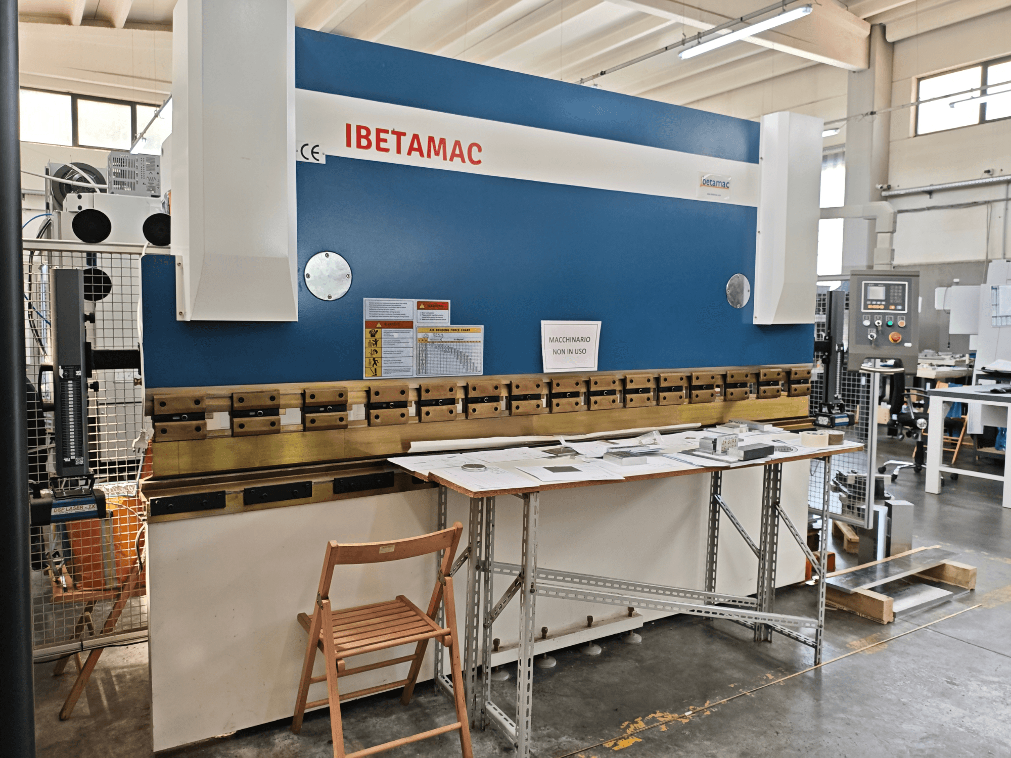 Plieuse IBETAMAC 3200 100T dans un atelier, vue de profil montrant le panneau de commande, la zone de travail et les consignes de sécurité.