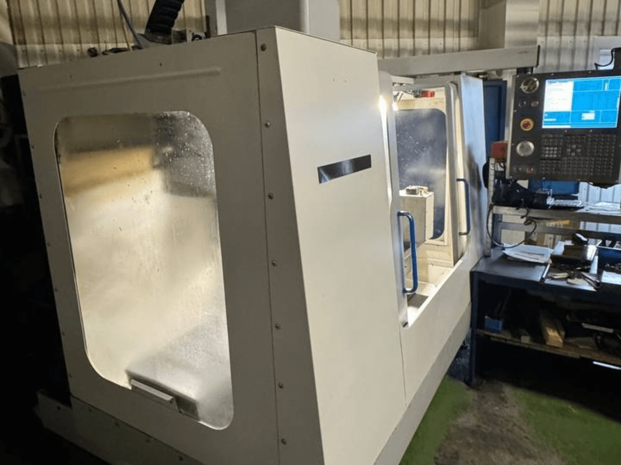 Centre d'usinage vertical HAAS VCE 750 en vue latérale, doté d'un panneau de commande et d'une enceinte de sécurité transparente.