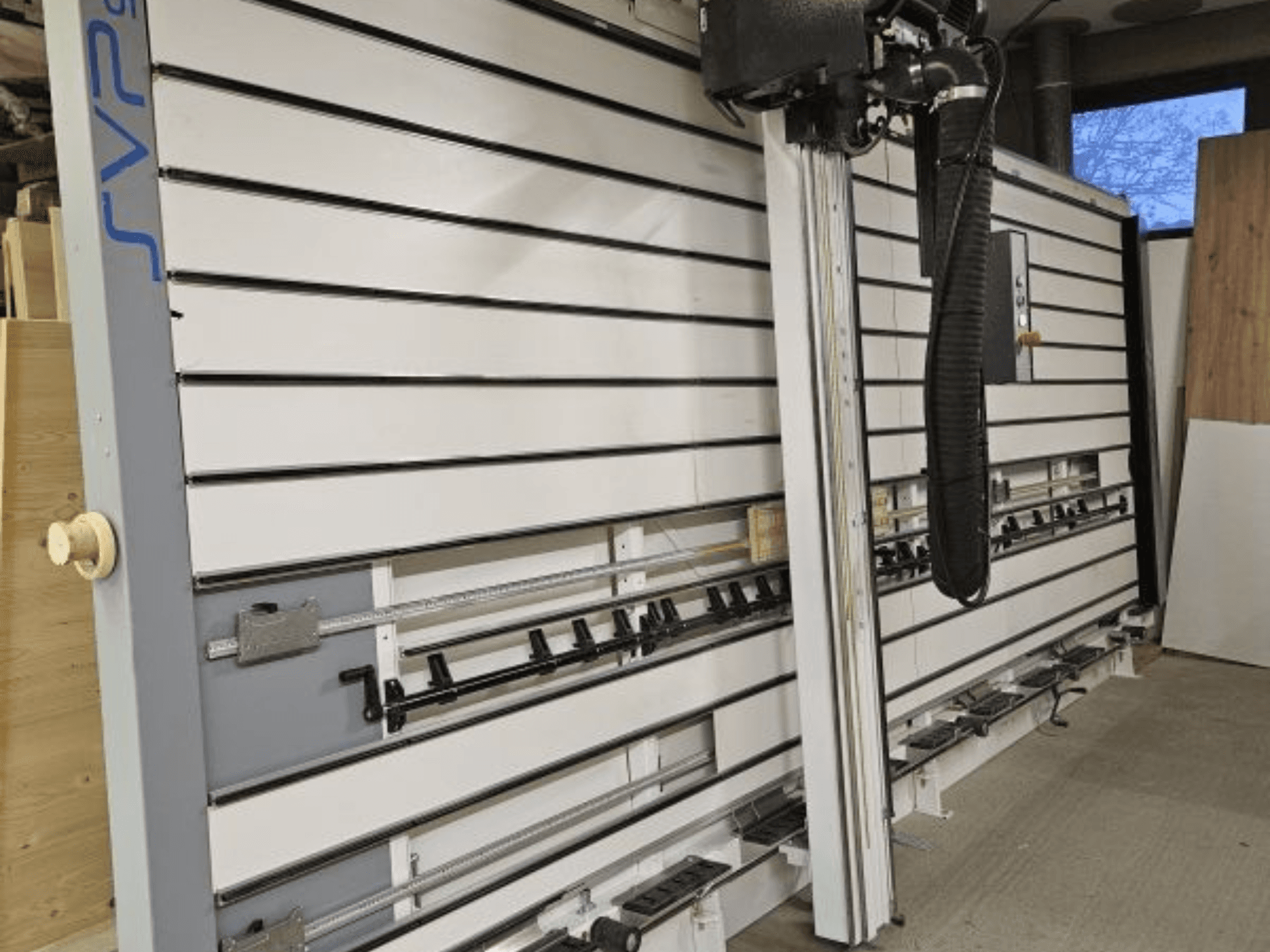 Scie à panneaux coulissante SVP dans un atelier, vue de face, équipée de rails réglables et d'un système d'aspiration des poussières en hauteur.