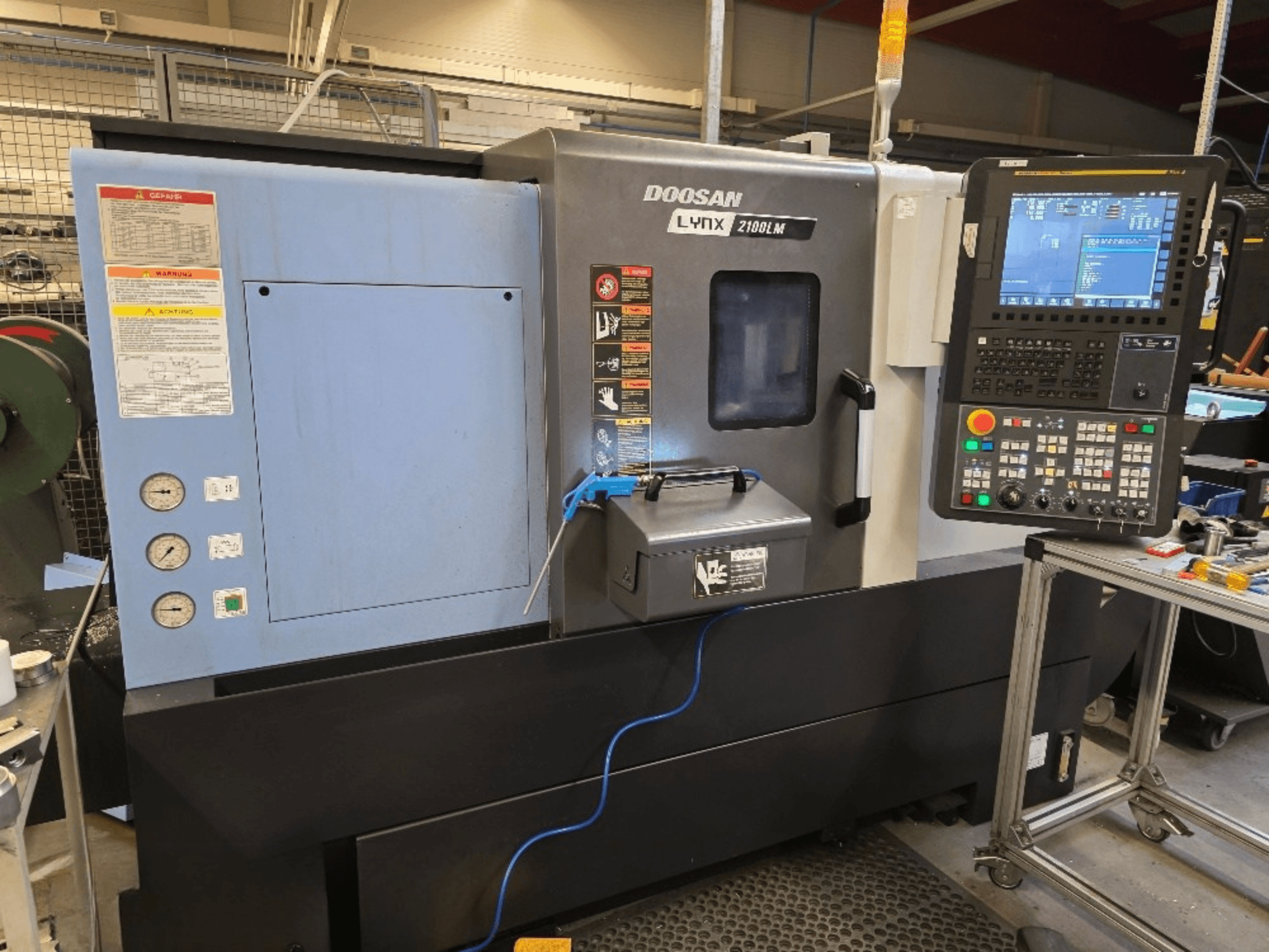 Tour CNC Doosan Lynx 2100LM, vue de face, avec panneau de commande, manomètres et avertissements de sécurité.