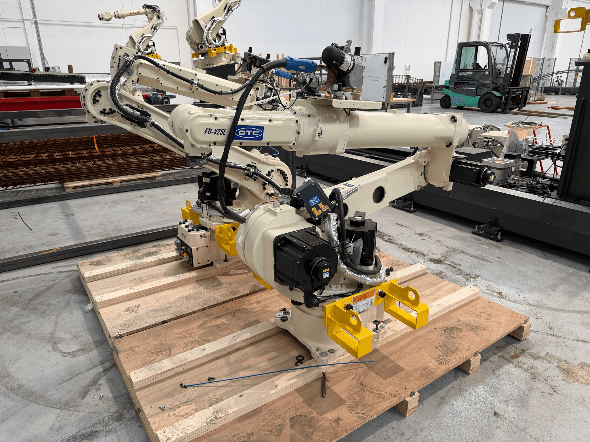 Bras robotique OTC Daihen FD19-V25L vu de face, doté de griffes de préhension jaunes et de composants mécaniques apparents, posé sur une palette en bois.
