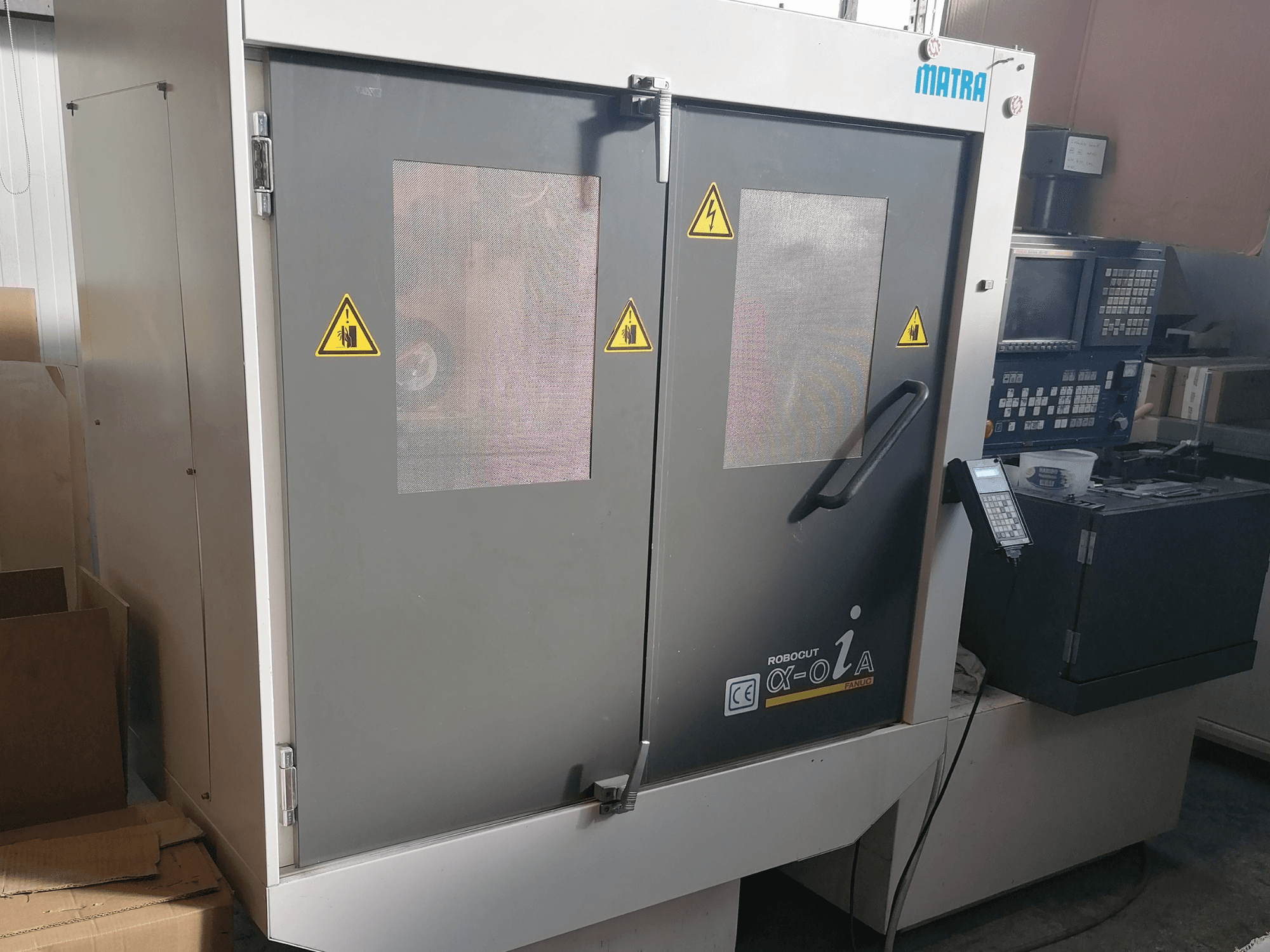 Machine Robocut α-oZα de Matra, vue de face montrant les avertissements de sécurité, le panneau de commande et les deux portes avec fenêtres en treillis.