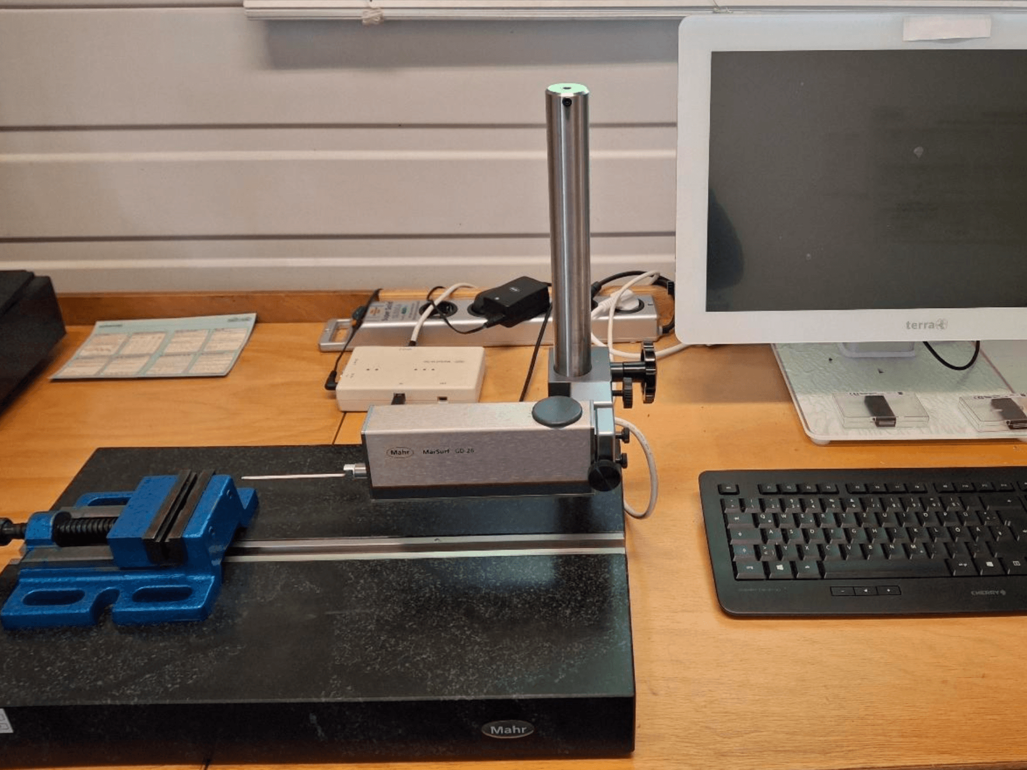 MAHR MARSURF GD 26 CMM sur un établi, avec un palpeur de mesure, un étau bleu et un écran d'ordinateur. Vue de face.