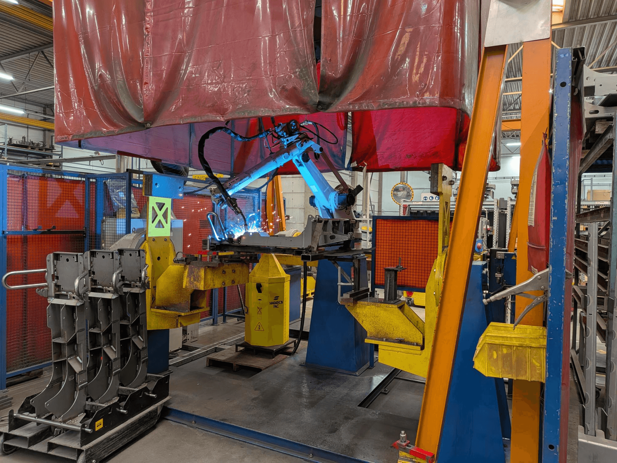 Le robot de soudage OTC Daihen DR4200 en action, vu de face, avec son arc de soudage bleu vif et son capot de protection.