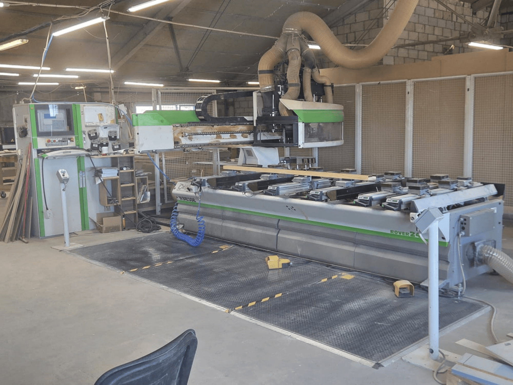 Centre d'usinage CNC BIESSE Rover 24S dans un atelier, avec un panneau de commande et une grande surface de travail avec des pièces en bois.