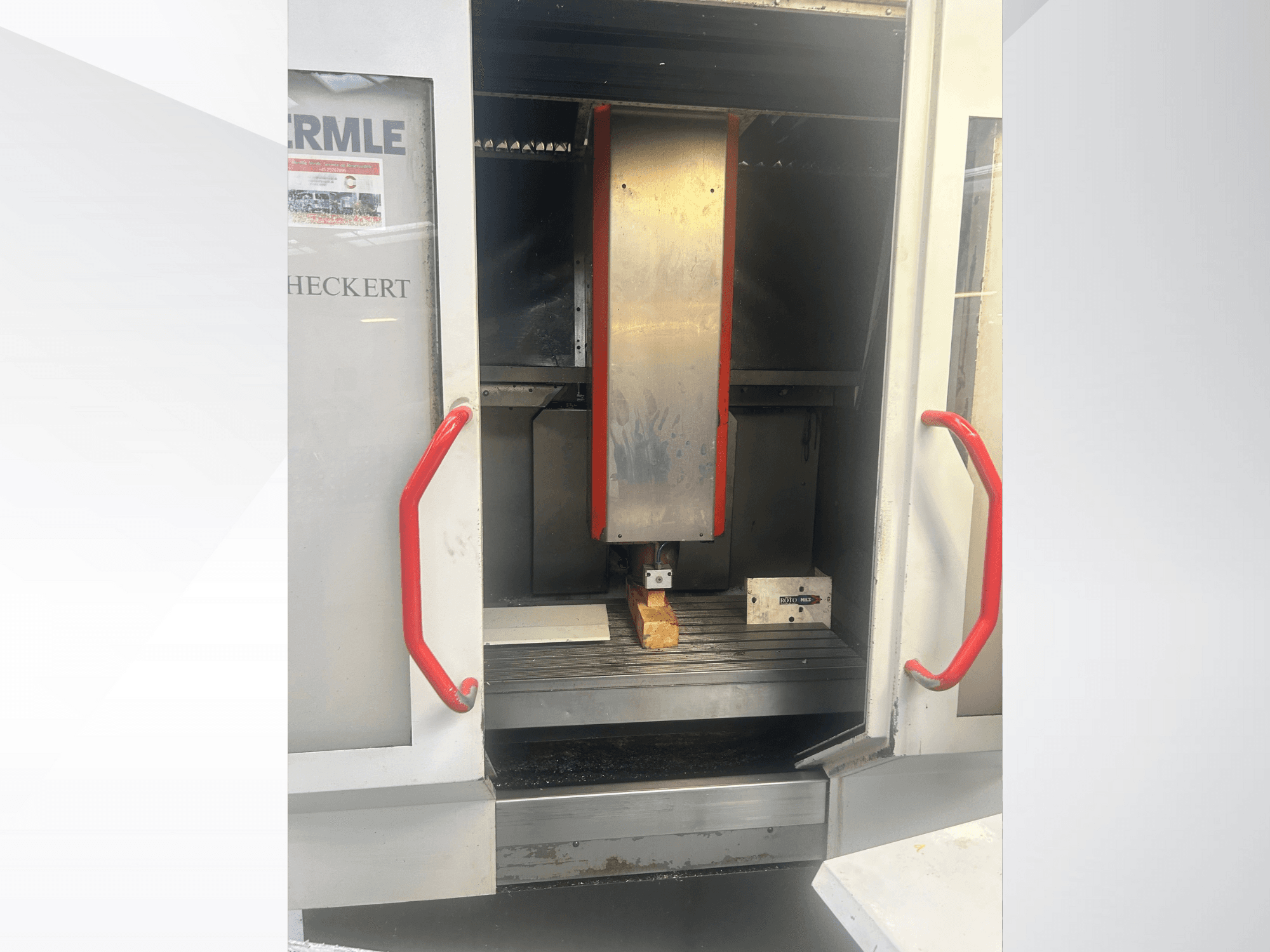 Machine CNC Hermle vue de face, avec un intérieur métallique, des poignées rouges et une pièce à usiner sur la table.