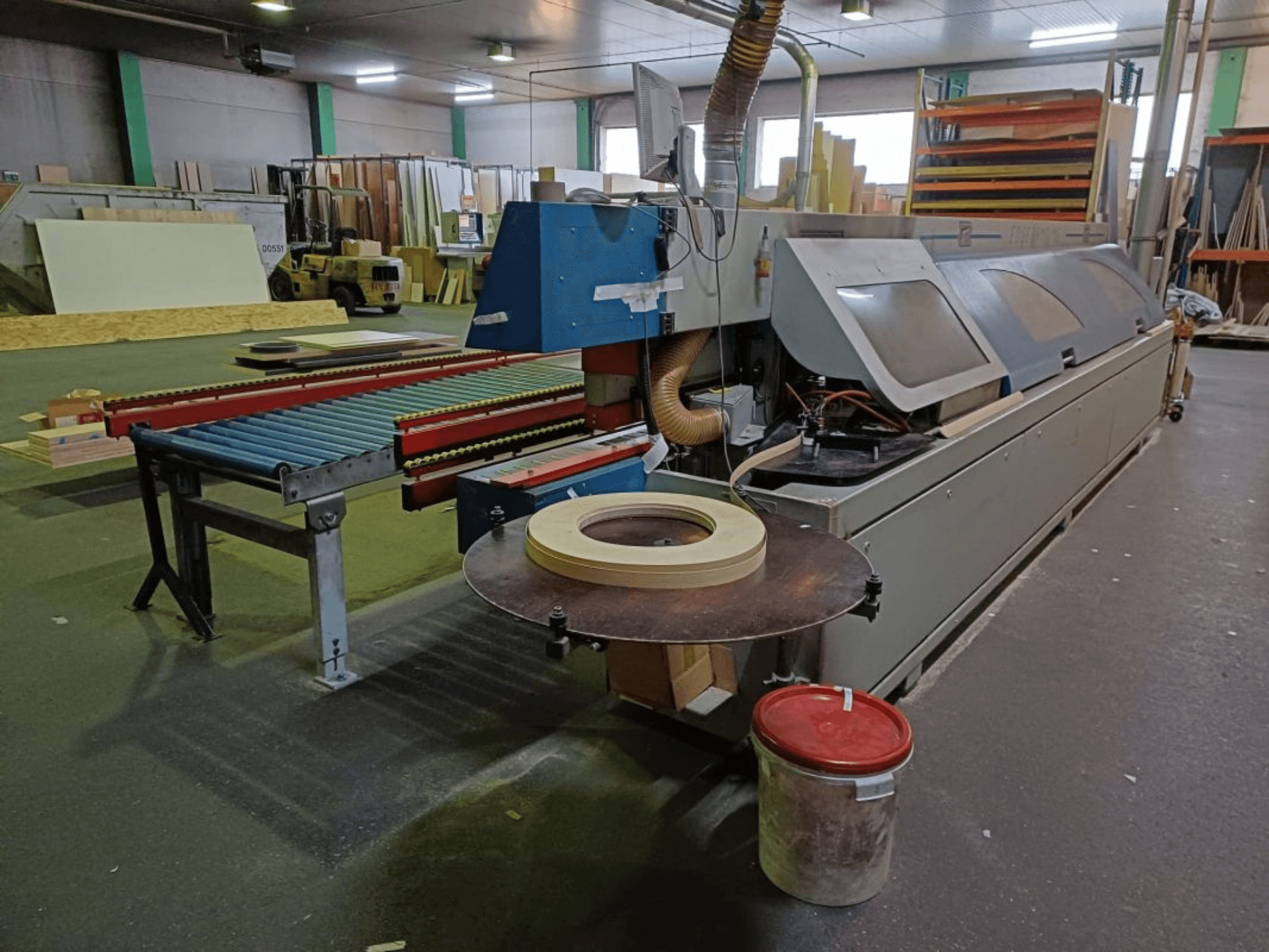 Plaqueuse de chants OTT TWISTER dans un atelier, avec un convoyeur à rouleaux et une scie circulaire, vue de côté.