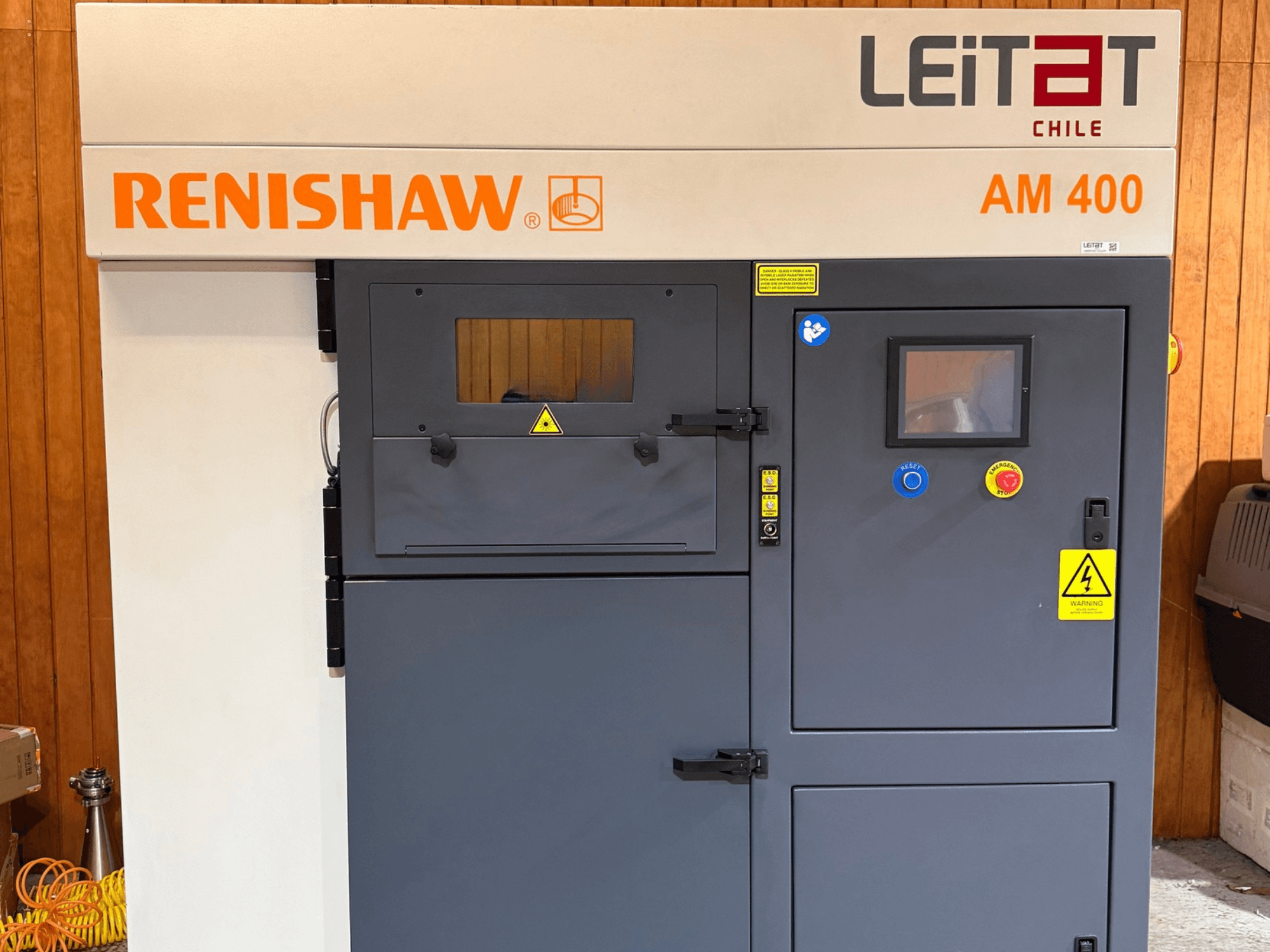 Vue de face de l'imprimante 3D métal RENISHAW AM400, avec son panneau de commande, ses étiquettes d'avertissement et son accès pour la maintenance.