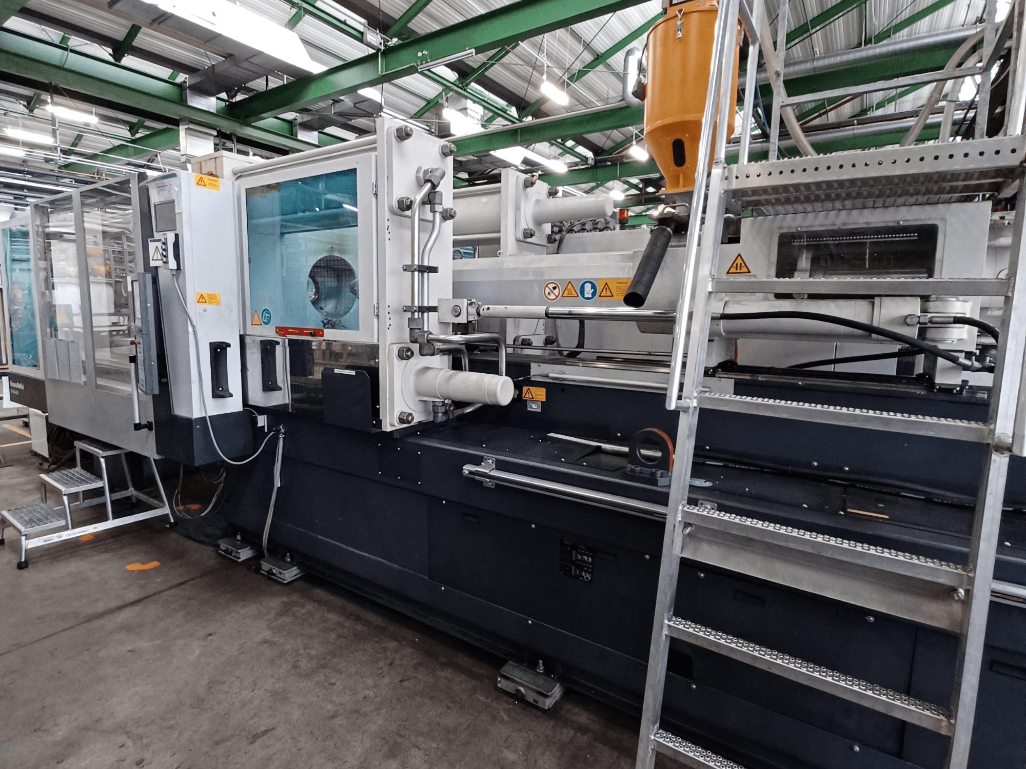 Machine de moulage par injection industrielle avec une vue frontale claire, montrant les marques, le panneau de commande et la trémie de matériaux.